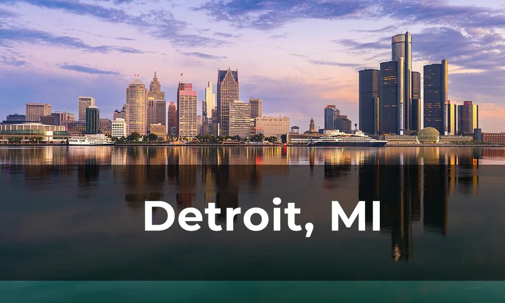 Skyline of Detroit, Michigan, with tall buildings and water reflecting the cityscape during sunset.
