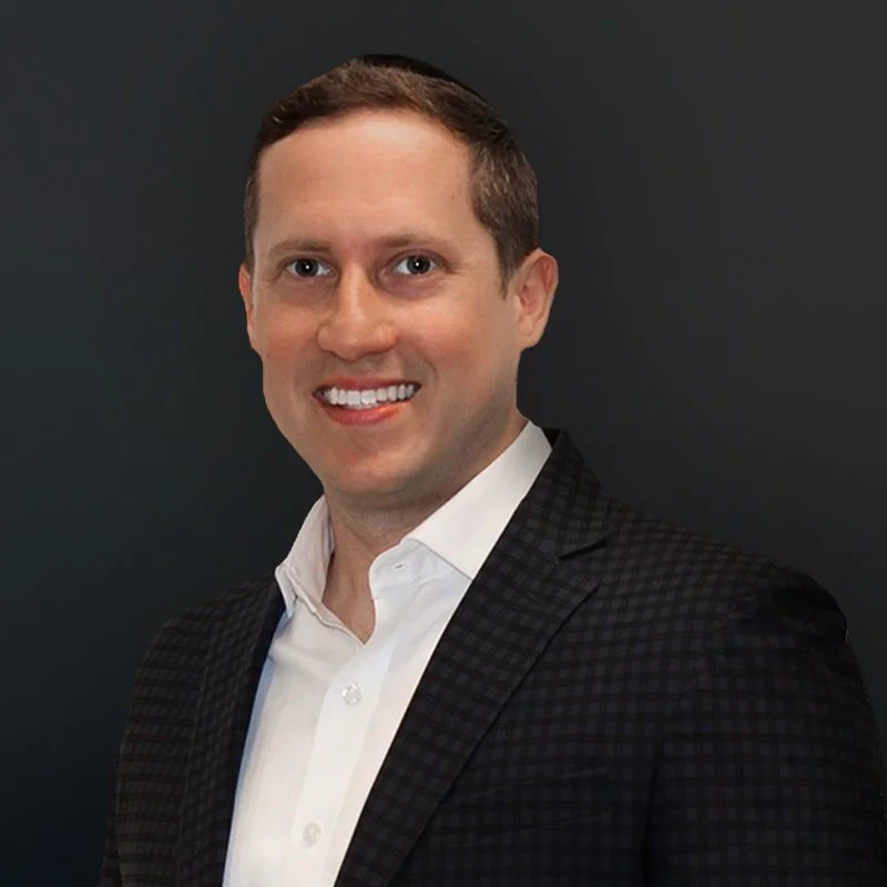 Man in a suit smiling against a dark background.