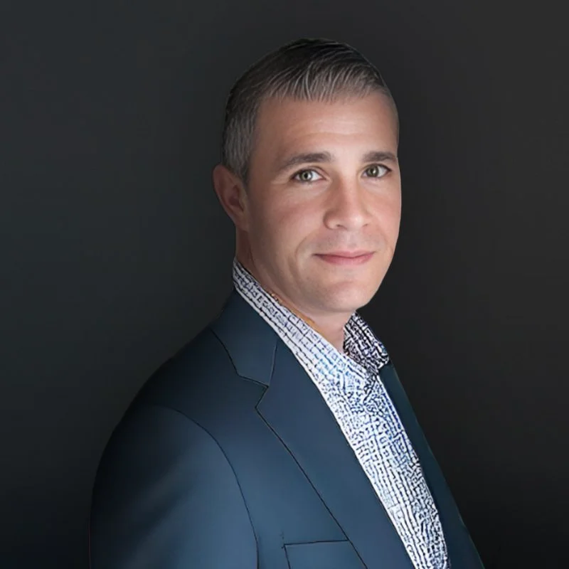 Man in a suit with a patterned shirt against a dark background.