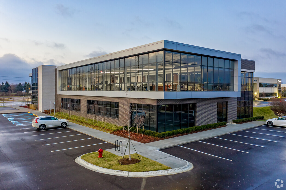 Modern office building with large windows, surrounded by a parking lot with a few cars, and a small landscaped area with a fire hydrant.