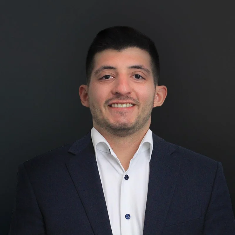 Man in a dark suit and white shirt smiling against a black background.