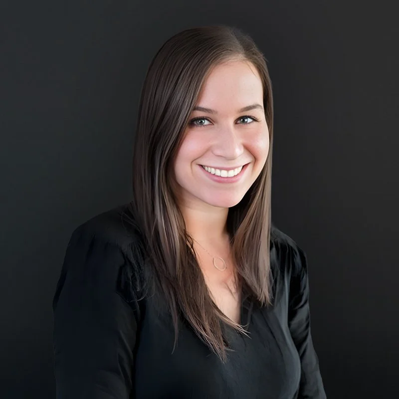 A young woman with long brown hair and blue eyes smiling against a black background.