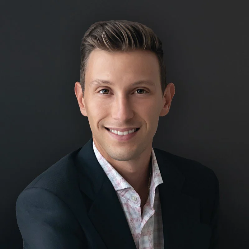 A smiling man in a suit with a dark background.