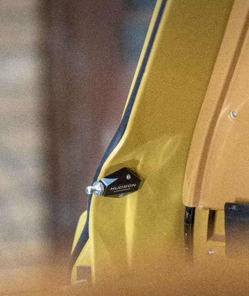 Close-up of a yellow electric guitar with a black strap button and a black strap with the word 'HUDSON' printed on it.