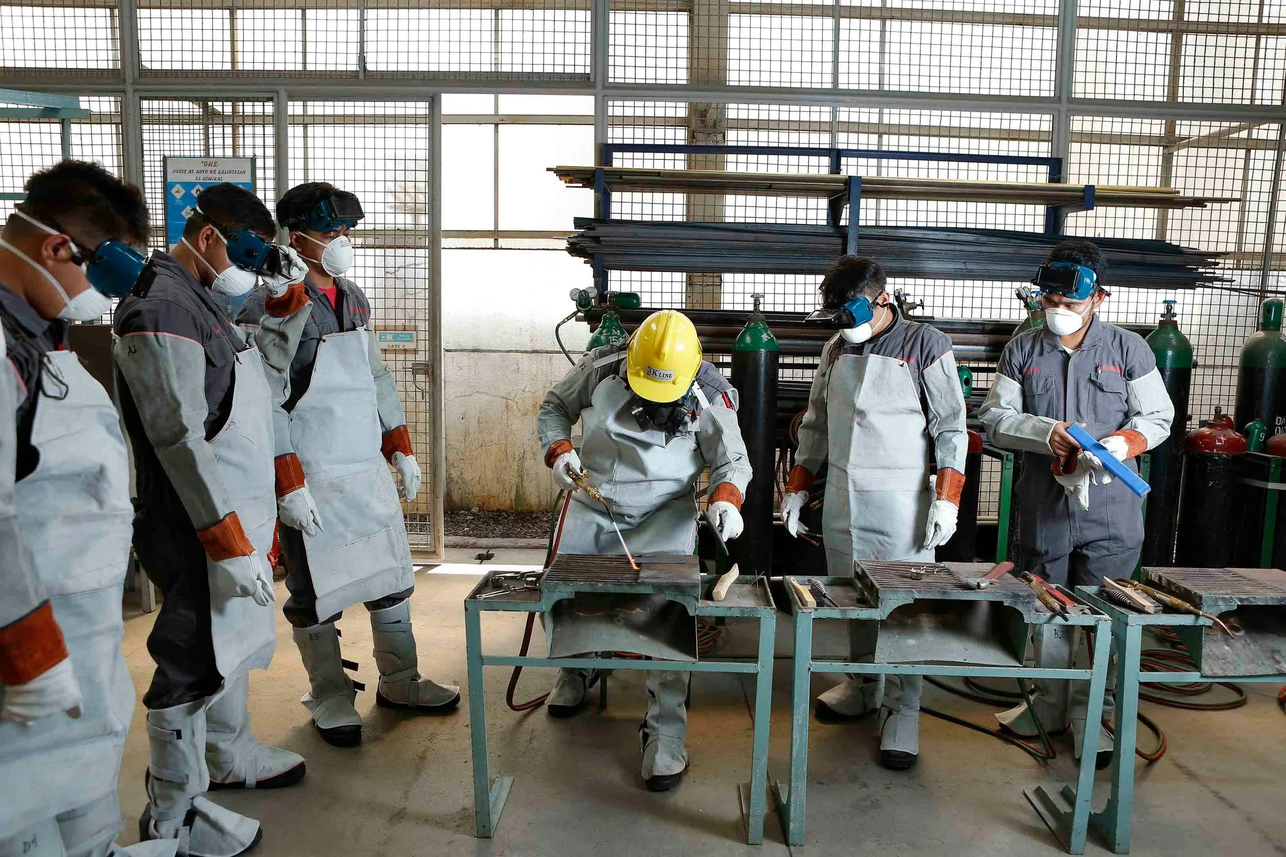 Group of workers in safety gear and face masks working with welding tools in an industrial workshop.