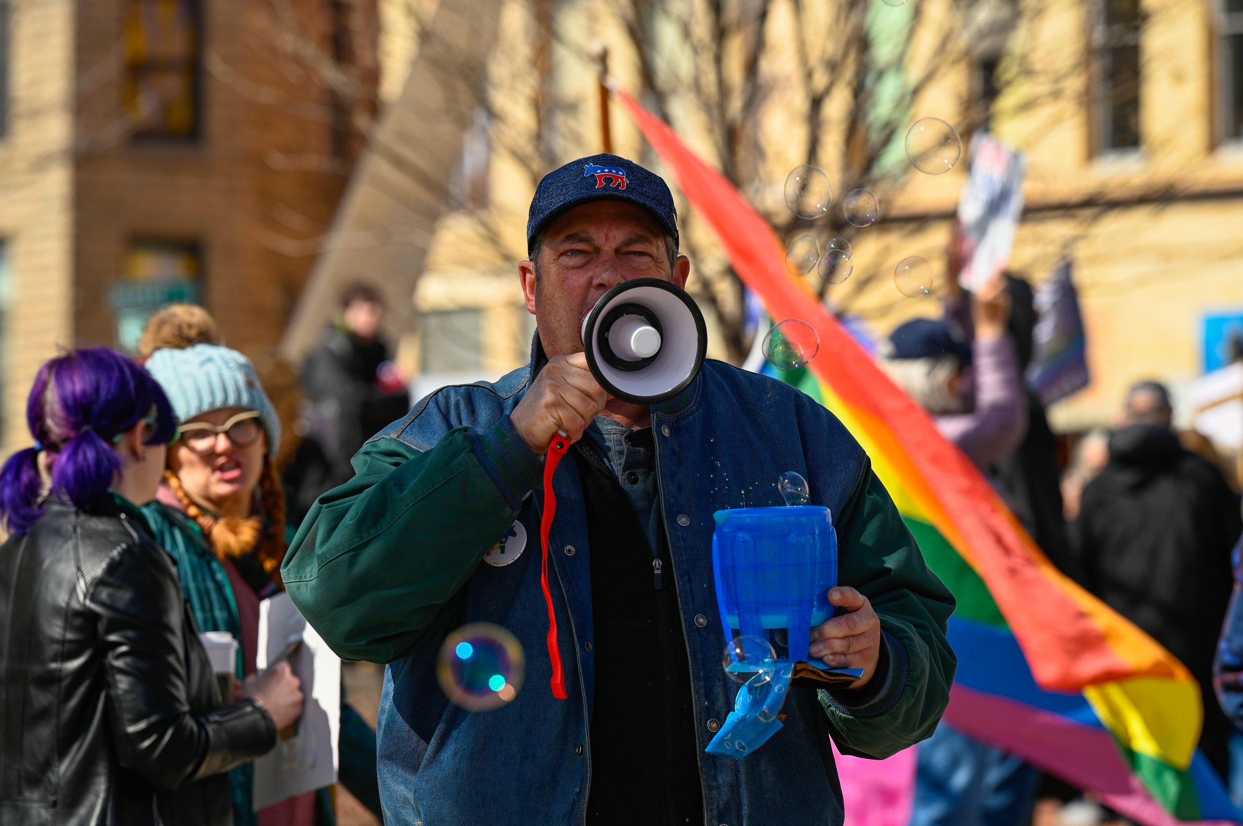 A man shouts into a megaphone while holding a bubble machine at Opera House Square in Oshkosh, Wisconsin, on April 5, 2025. State Representative Lori Palmeri attended the protest in Oshkosh and gave a speech in which she encouraged attendees to take