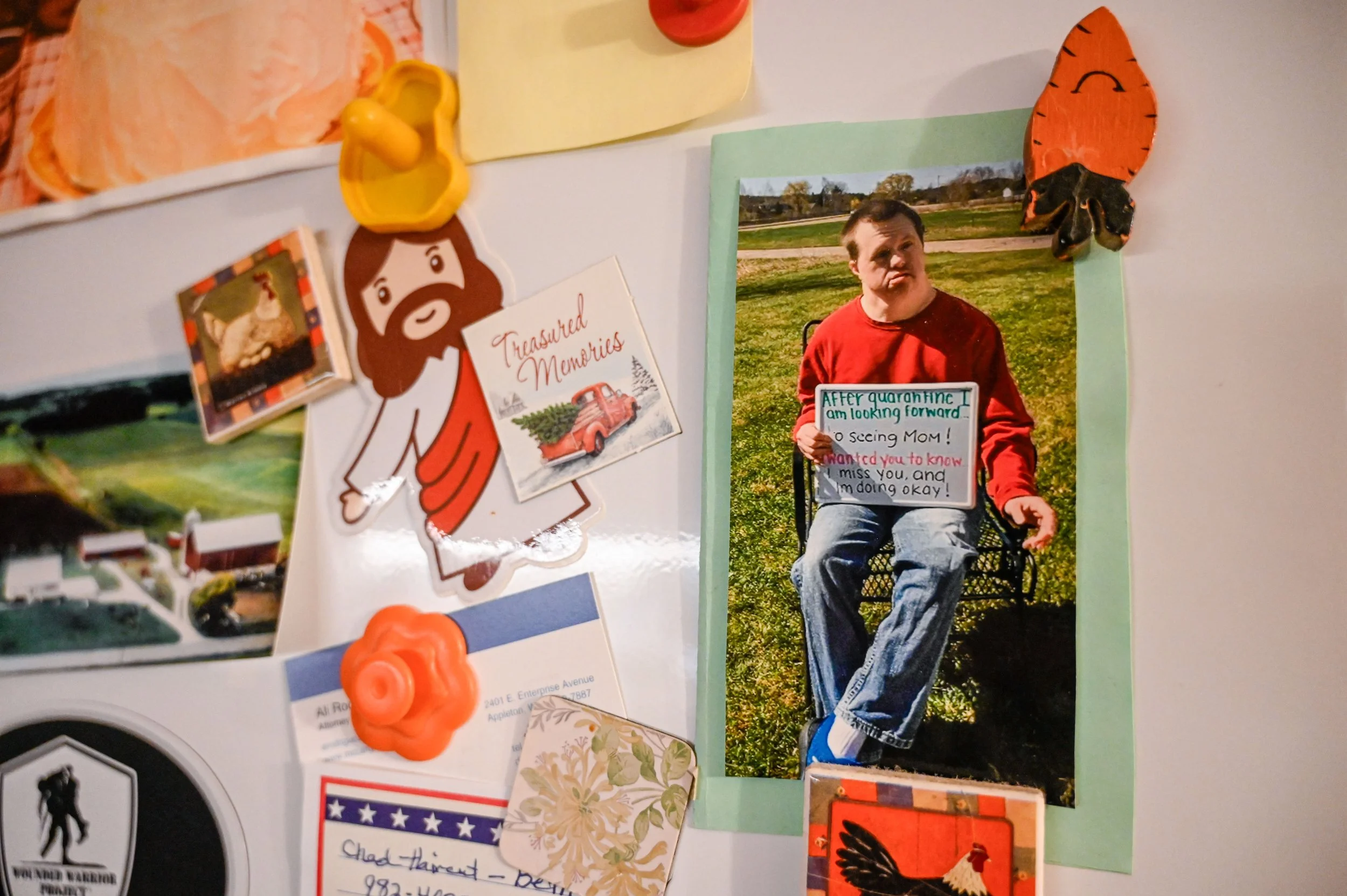 A photo of Chad hangs on the fridge. The sign he holds reads “After quarantine I am looking forward to seeing Mom! I wanted you to know I miss you, and I’m doing okay!” The photo was taken during the Covid-19 pandemic, while Chad was living in a grou