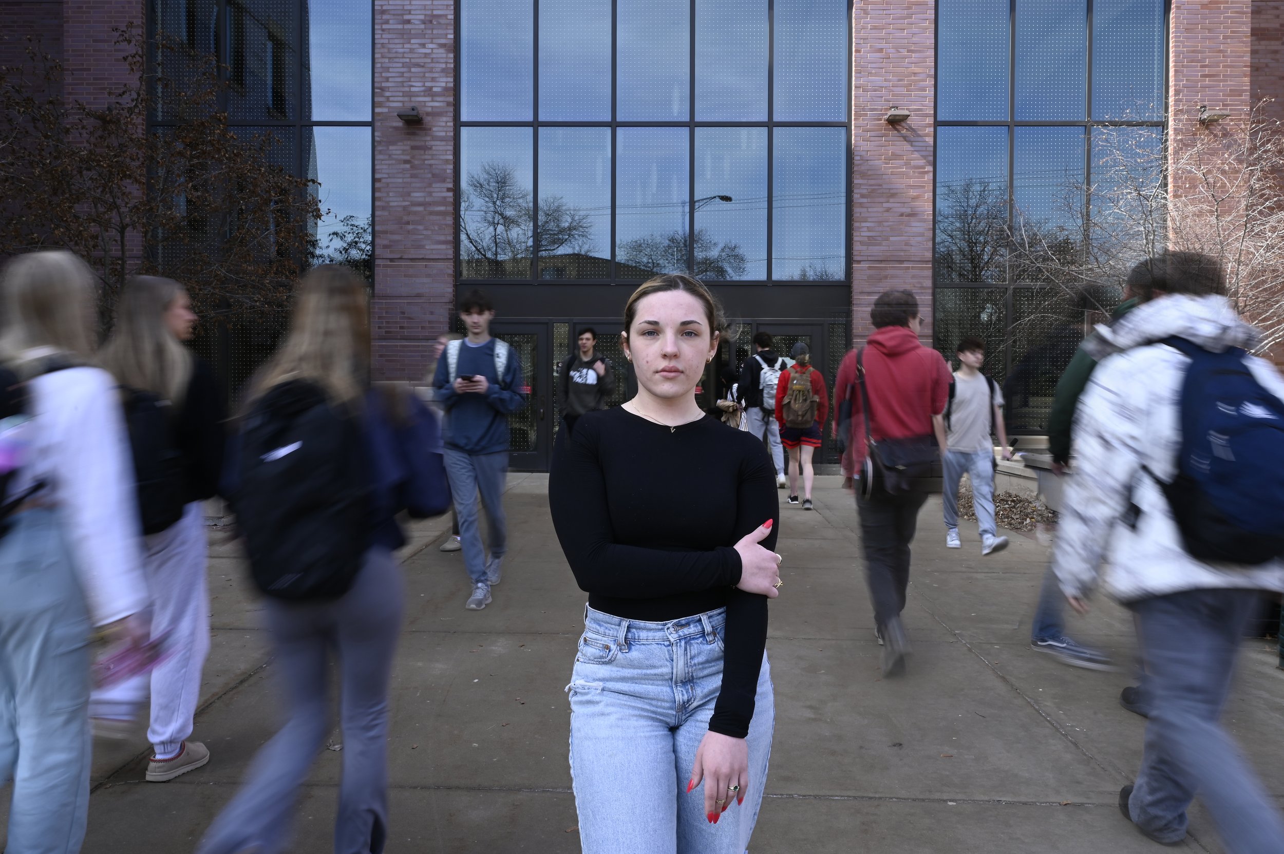 Nevaeh Serrano, a sociology student at UW-Oshkosh, stands in front of Sage Hall as other students pass her in Oshkosh, Wisconsin, on March 11, 2025. Serrano said the second Trump administration made her feel nervous and uncertain about the future. "D