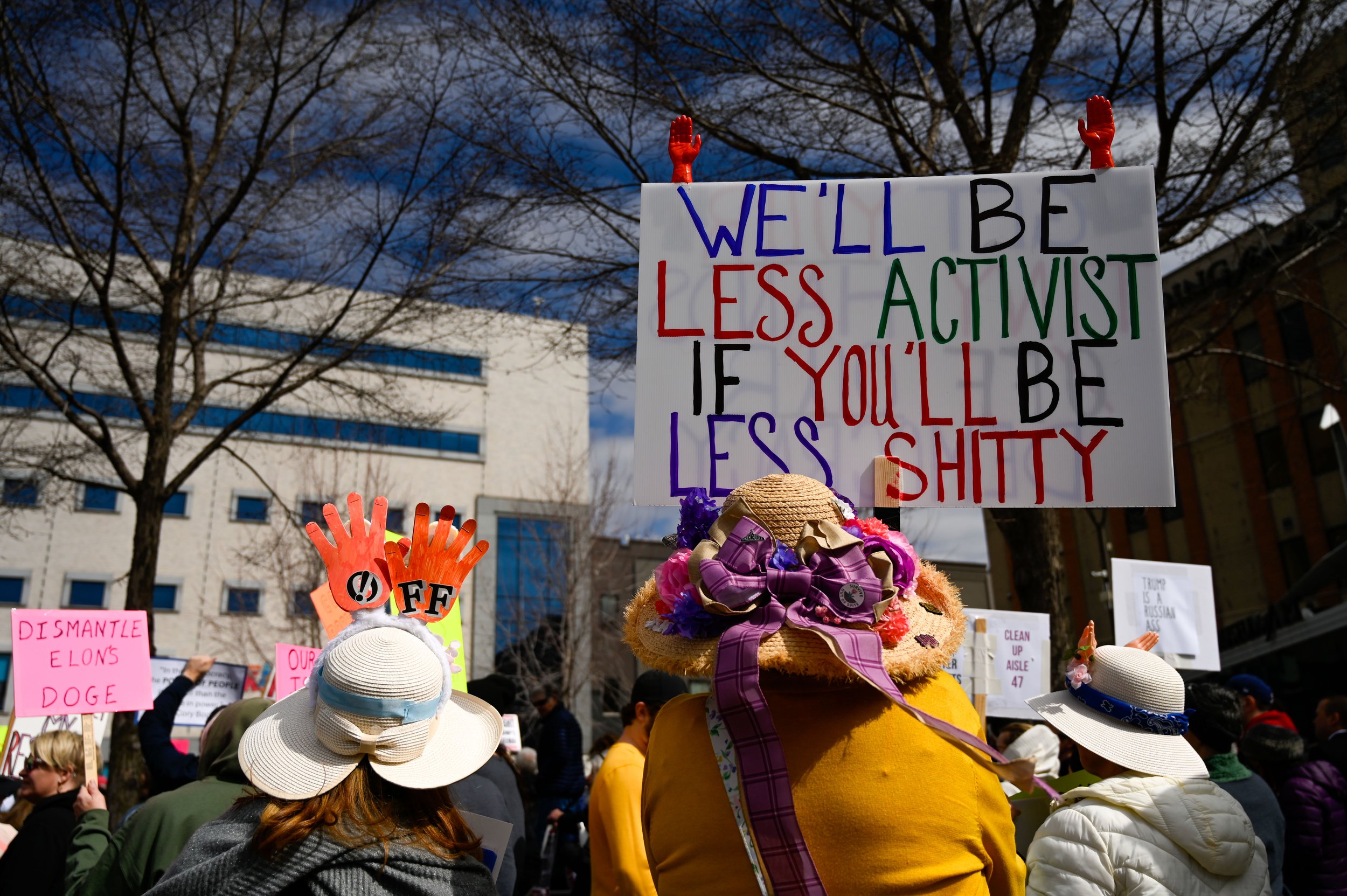 Three women wear elaborate sun hats as they listen to a speaker at Houdini Plaza in Appleton, Wisconsin, on April 5, 2025. Various forms of headgear have been worn in resistance throughout the decades. (Photo by Advance-Titan Photo Editor Jessica Duc