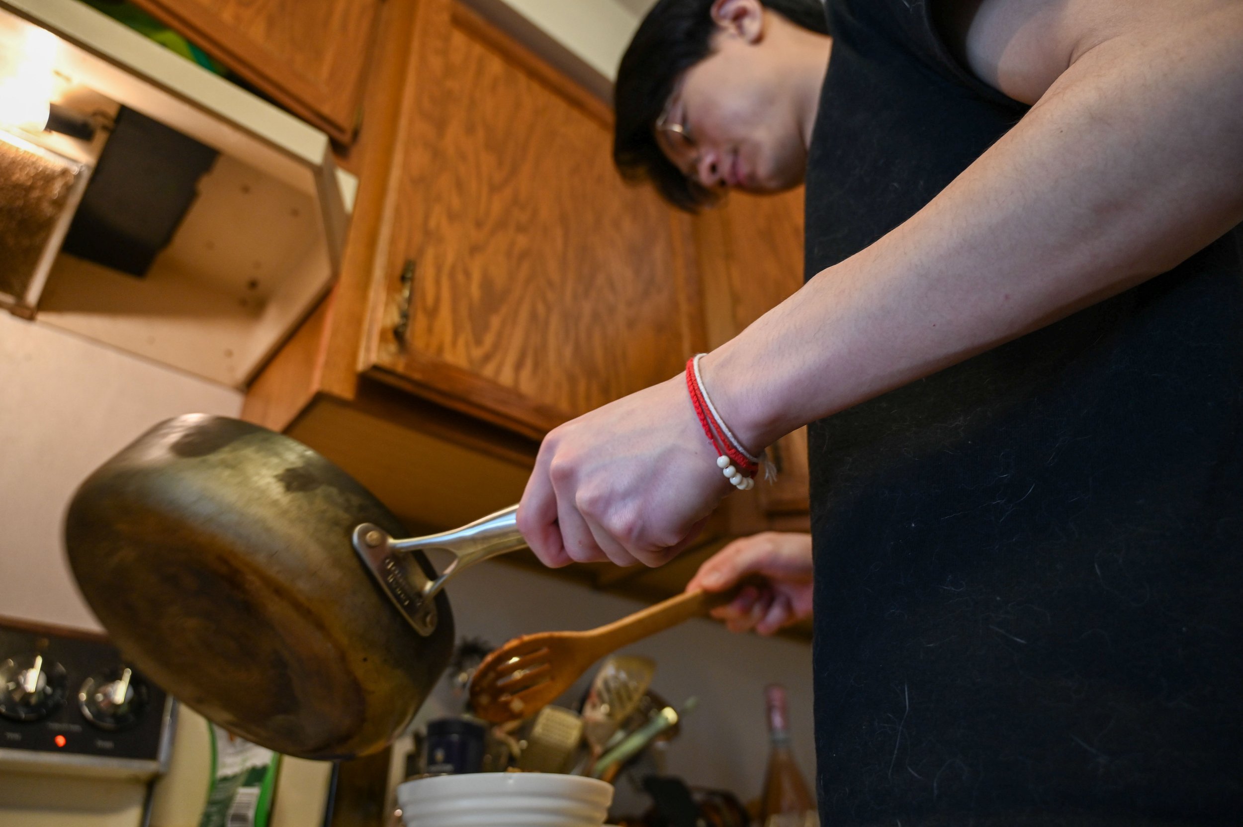 Kenneth Lee cooks breakfast for his girlfriend and wears a Sai Sin bracelet in Appleton, Wis., Tuesday, March 17, 2026. The bracelet is similar to the Hmong Khi Tes, but Lee received the blessing bracelet from his Laotian grandmother, who is buddhist