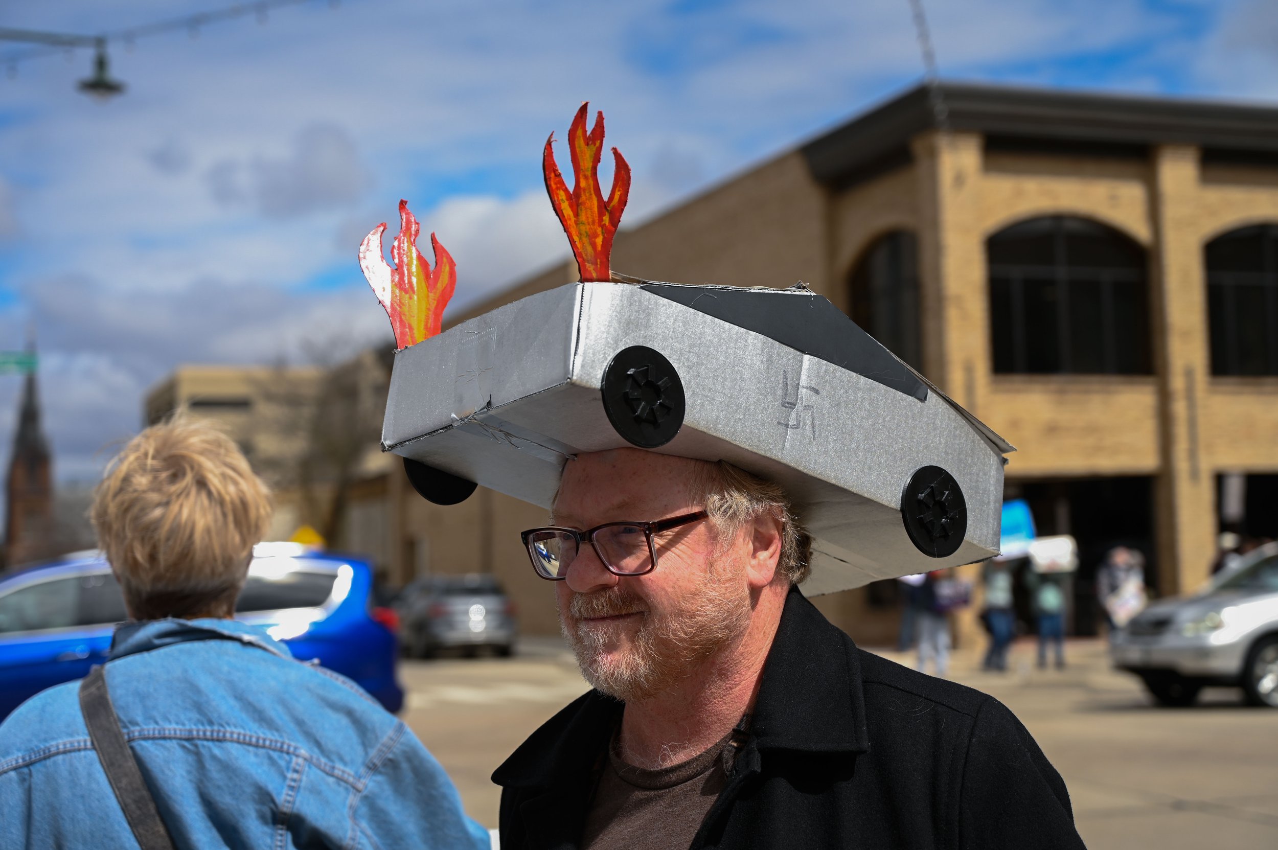 A man smiles while wearing a hat shaped like a Tesla Cybertruck with flames coming out of its hood at Houdini Plaza in Appleton, Wisconsin, on April 5, 2025. Tesla CEO Elon Musk’s Department of Government Efficiency has targeted Diversity, Equity and