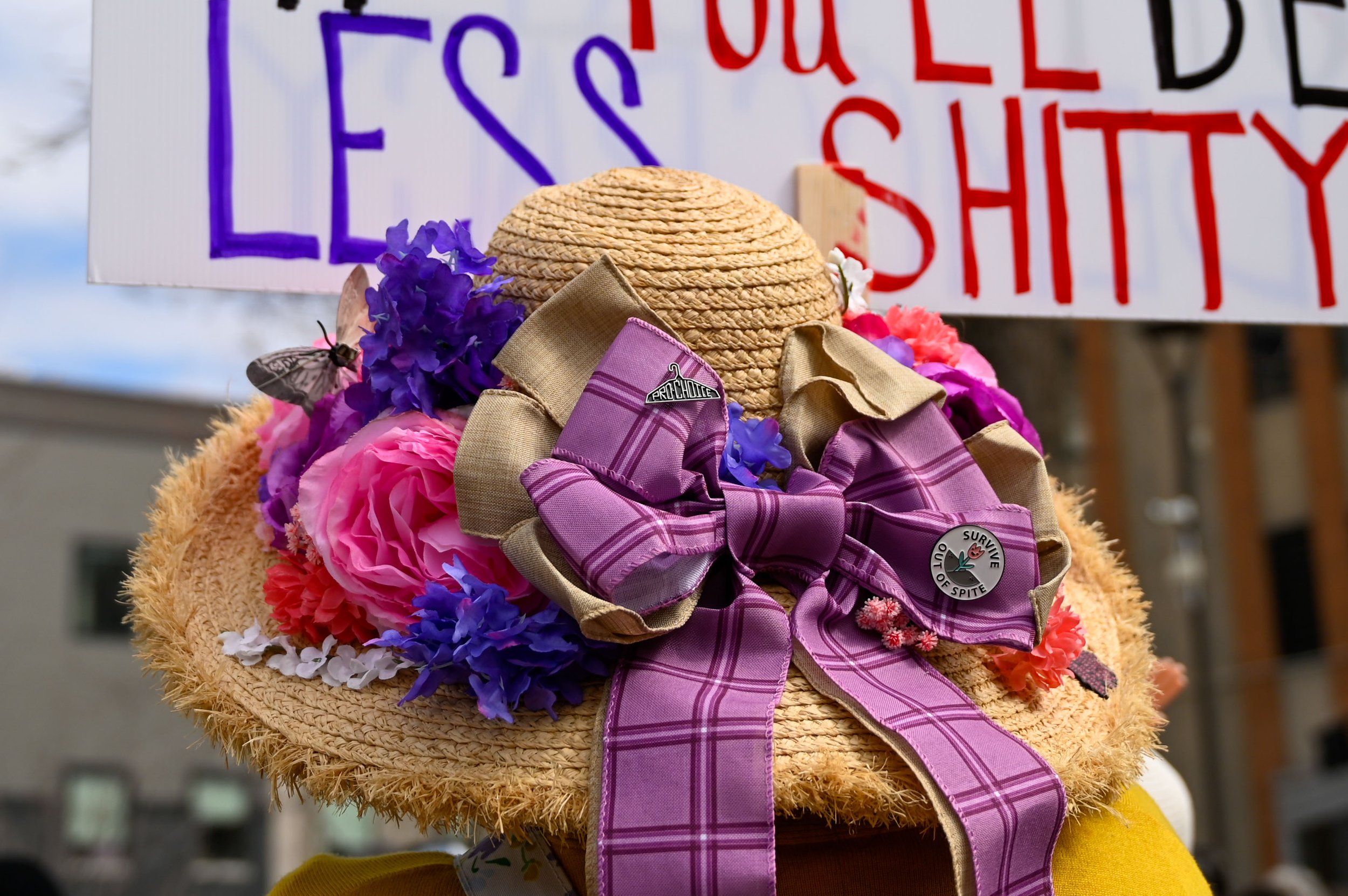 A woman stands with her friend and listens to a speaker at Houdini Plaza in Appleton, Wisconsin, on April 5, 2025. Her was adorned with flowers and two pins, one that said "Pro Choice," and other that said "Survive out of Spite." (Photo by Advance-Ti