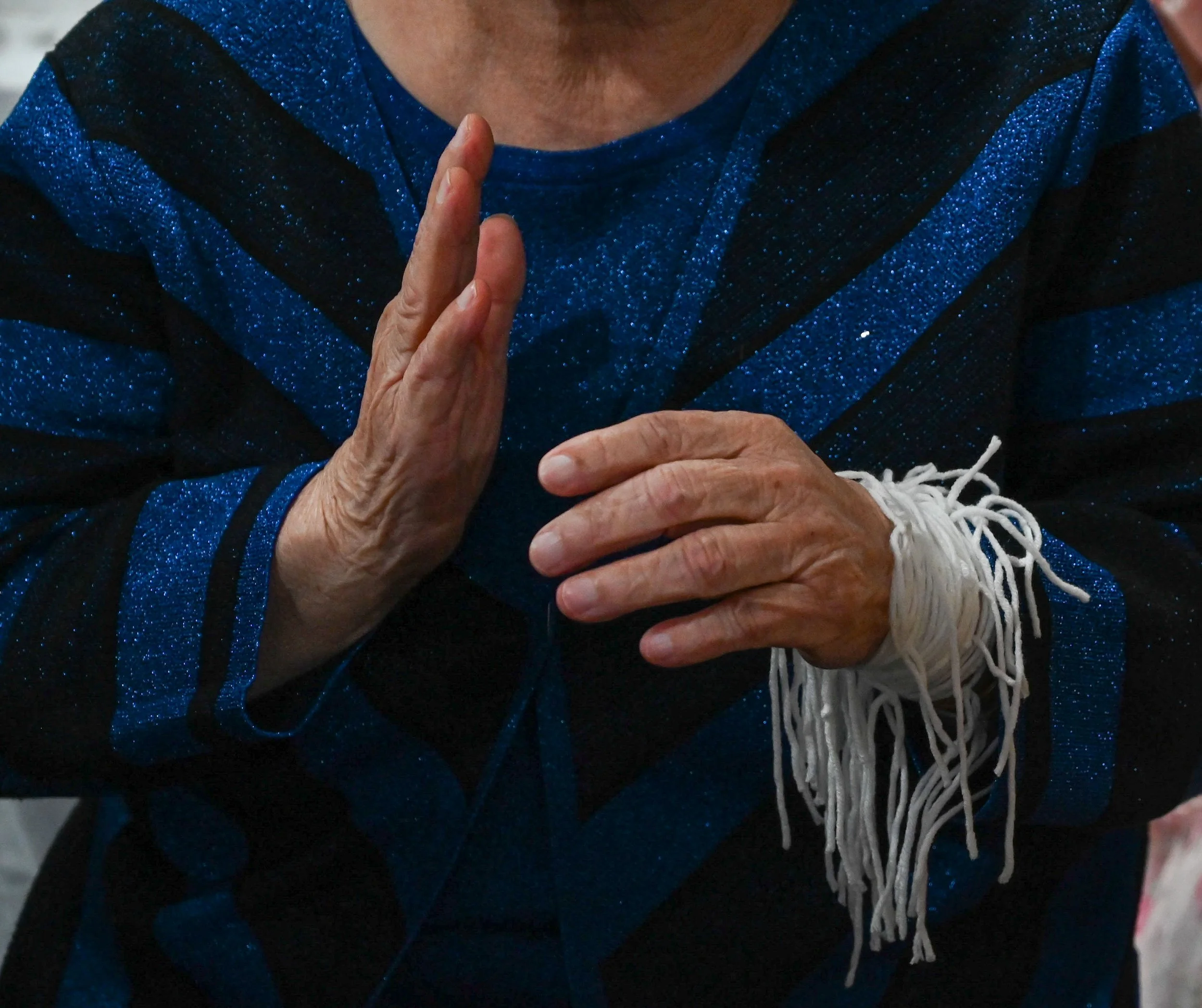 A woman holds out her hand during "Khi Tes" or hand-tying at a Hmong name-change ceremony in La Crosse, Wis., Saturday, April 18, 2026. The white strings symbolize blessings and good health.