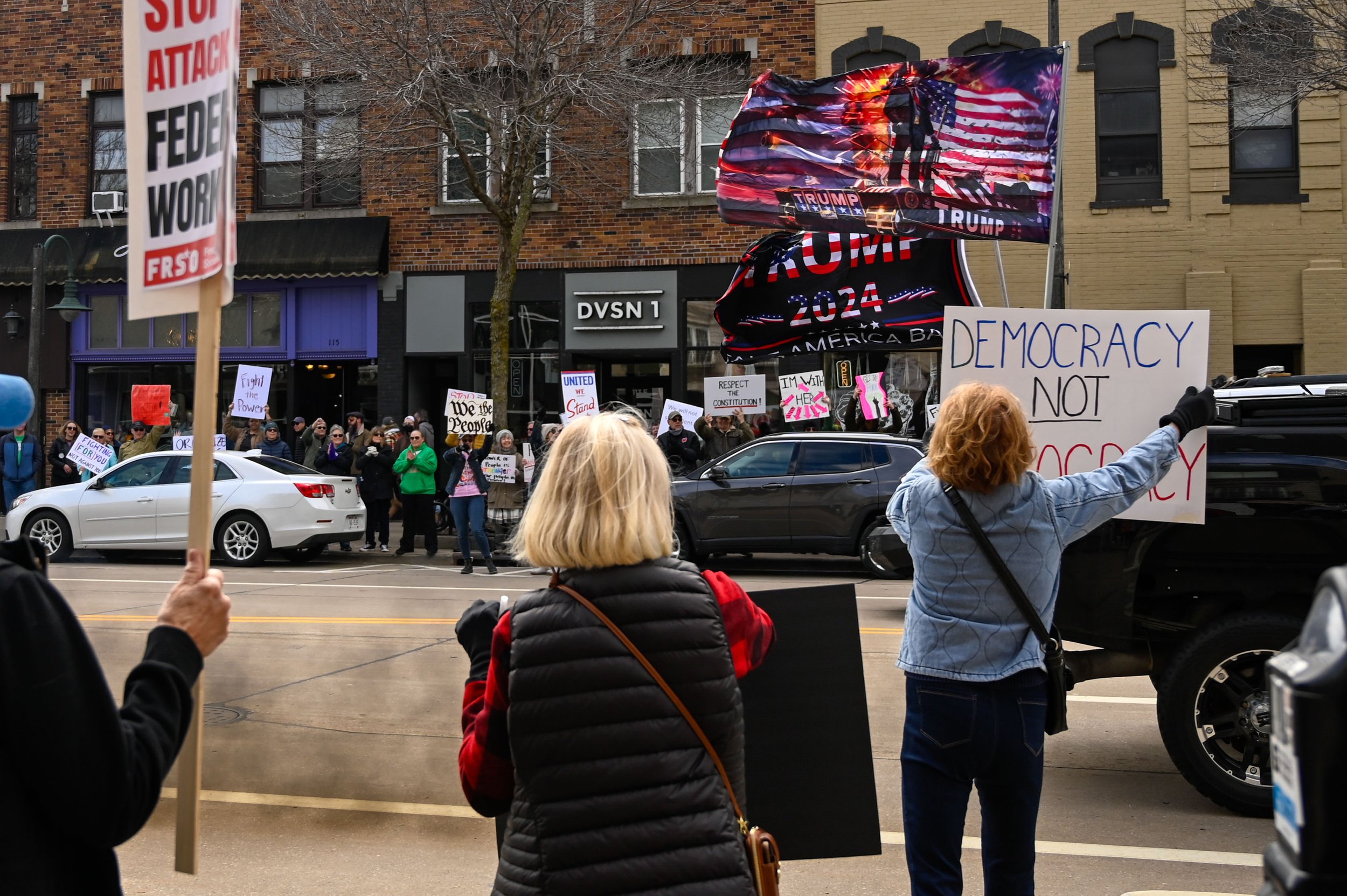 Protesters at the "Hands Off!" rally lunge toward a passing truck flying "Trump 2024" flags and throwing out smoke from its exhaust at Houdini Plaza in Appleton, Wisconsin, on April 5, 2025. Trump has issued over 100 executive orders since taking off