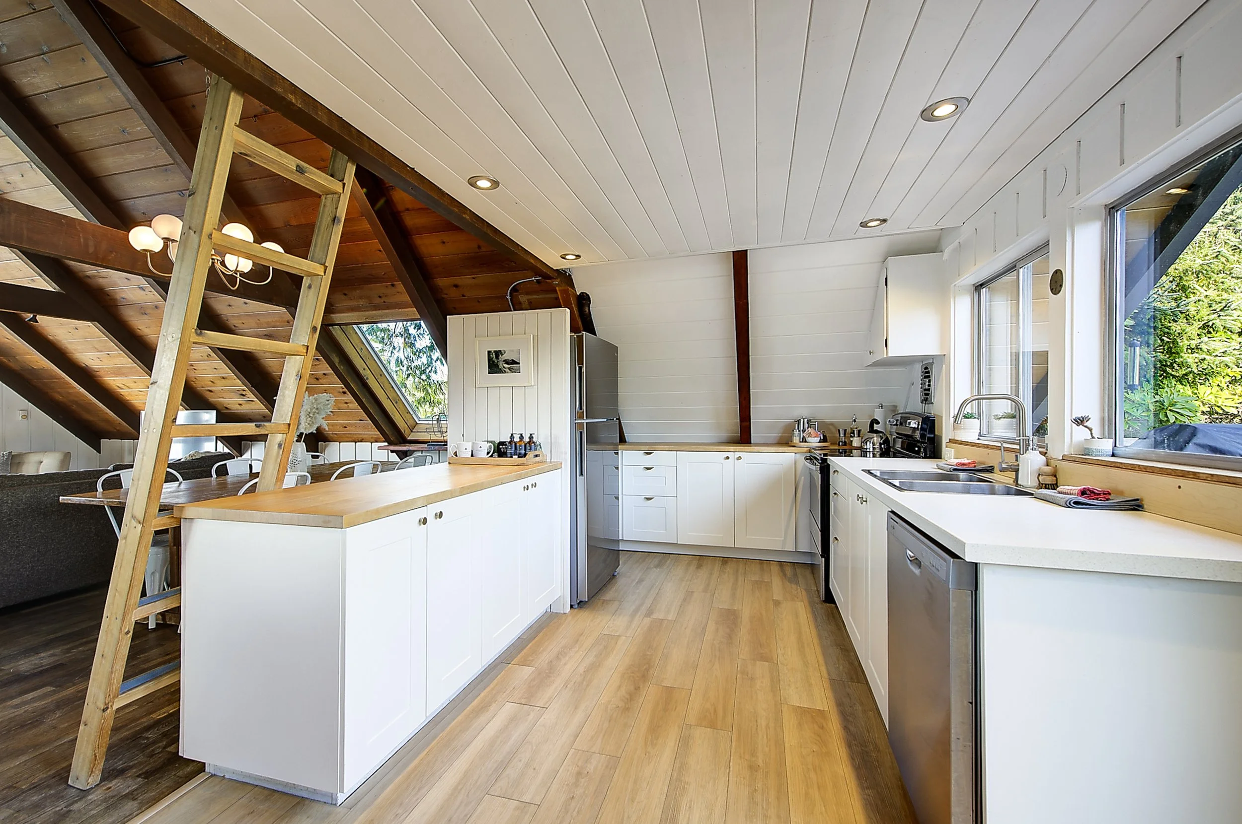 Modern kitchen with white cabinets, wooden countertops, large windows, and a sloped ceiling with installed recessed lighting.