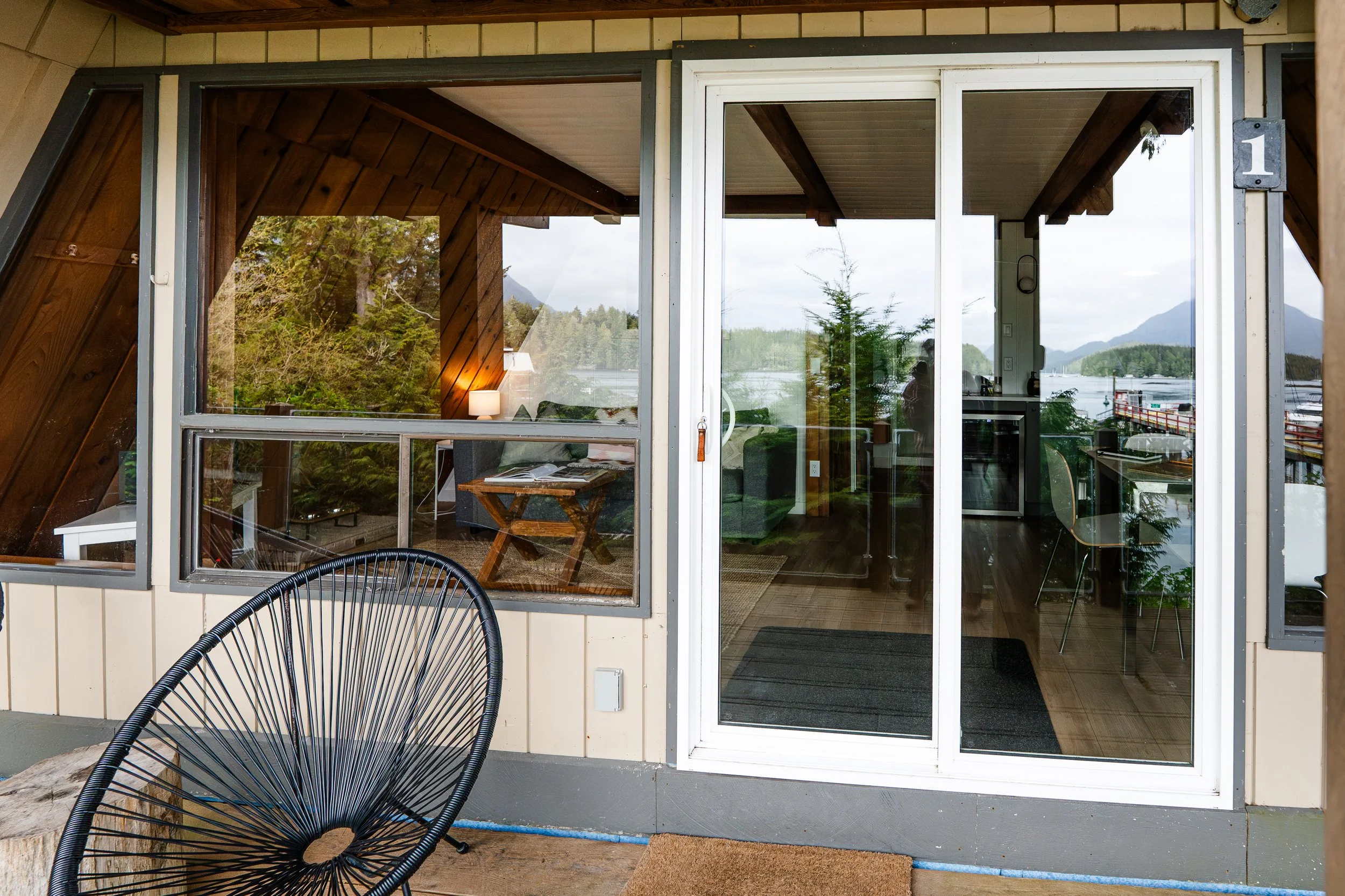 A view of a house patio with large sliding glass doors, showing a cozy living room and a scenic outdoor landscape with trees and mountains in the background.