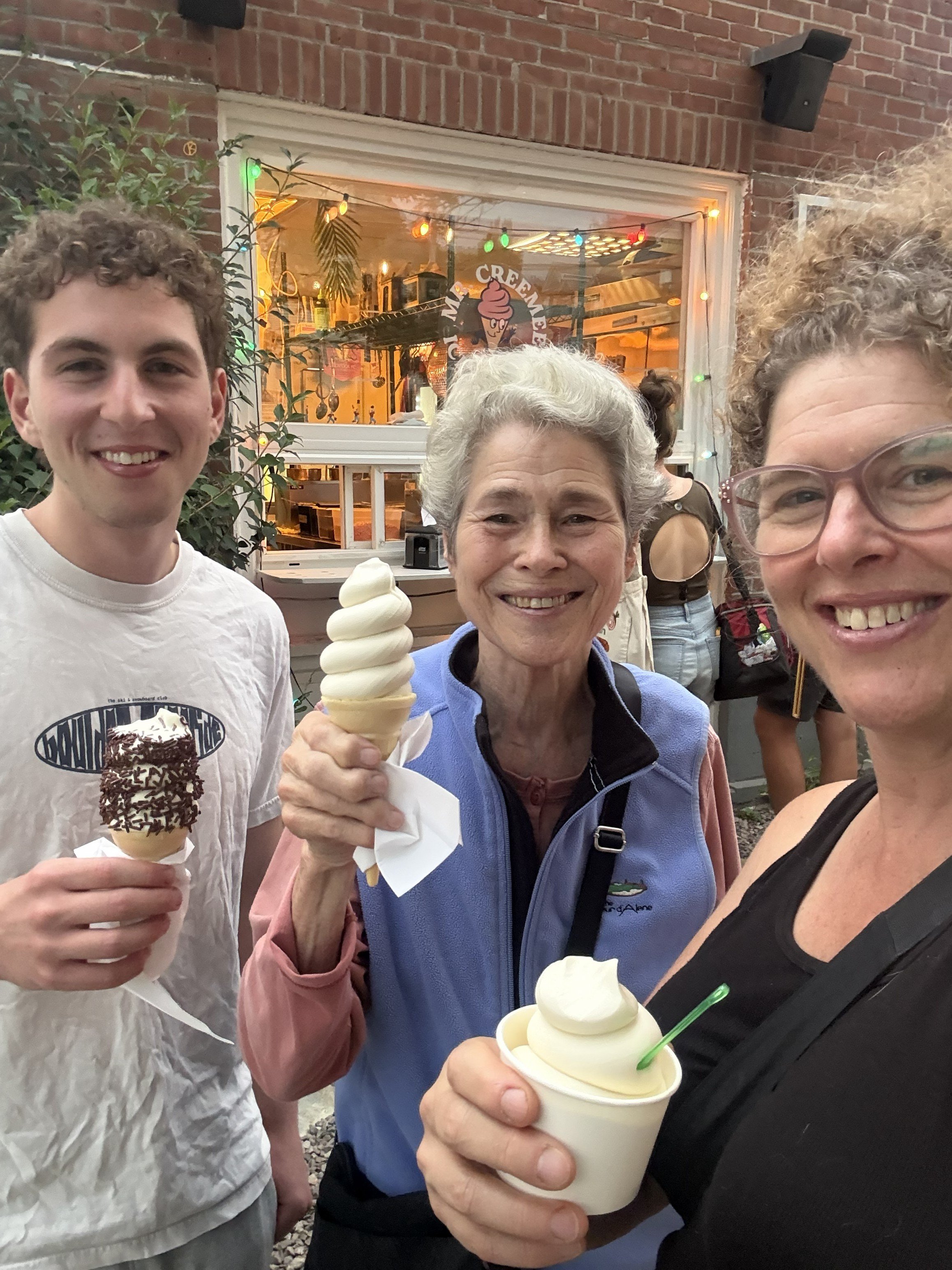 Three white people holding soft serve ice cream and smiling. It is a young adult, his mom, and his grandmother.