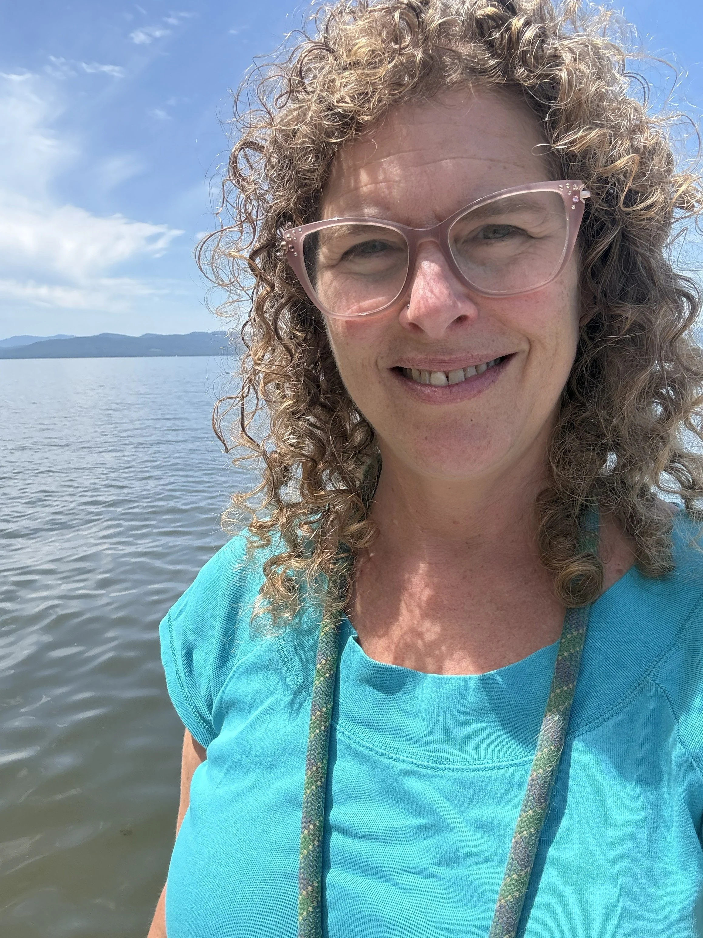 Rachel Siegel, a white woman with curly brown hair and glasses, stands in front of a lake.
