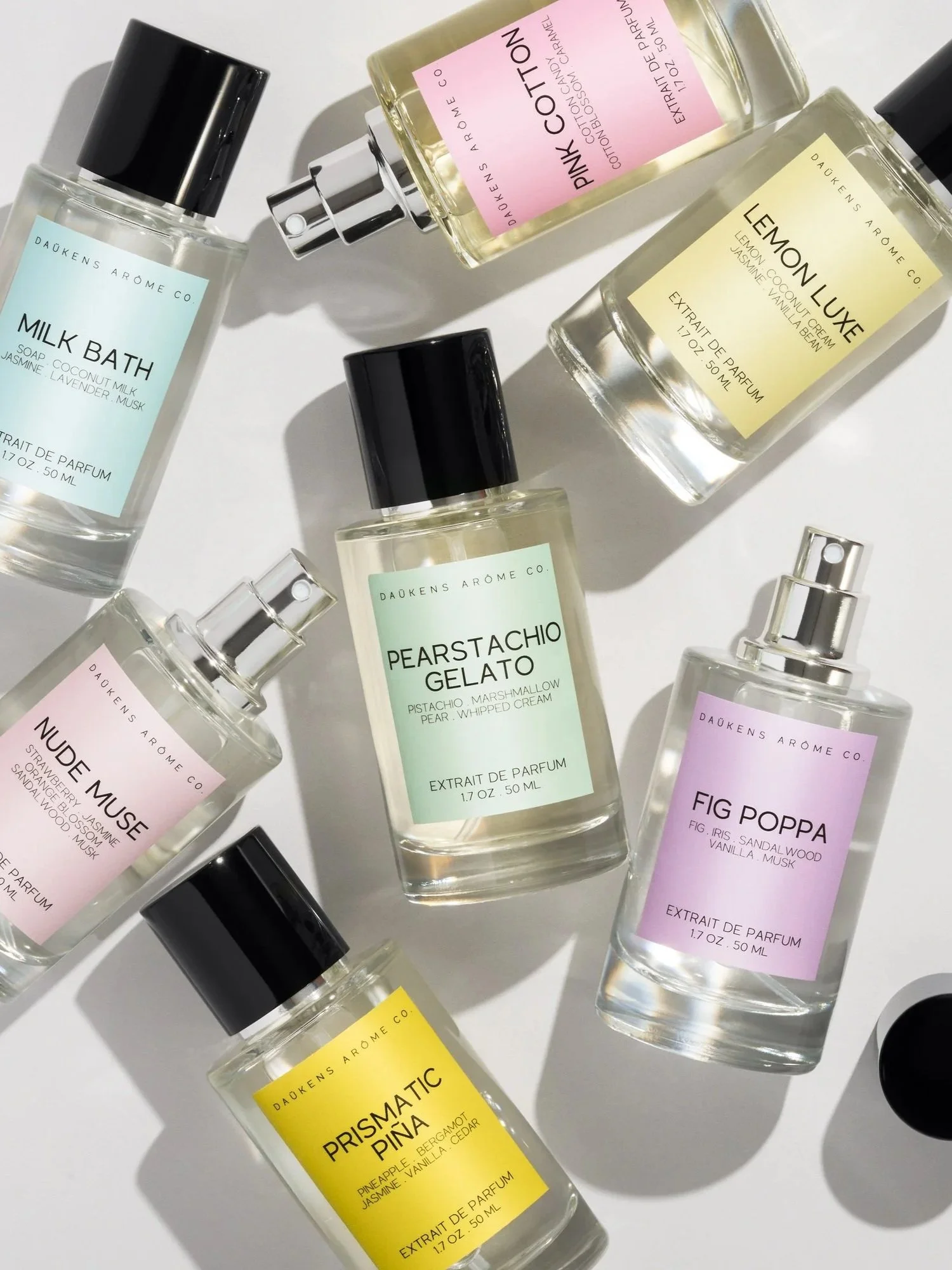 Collection of perfume bottles with pastel labels and black caps on a white background, some with spray nozzles and one with a black circular cap.