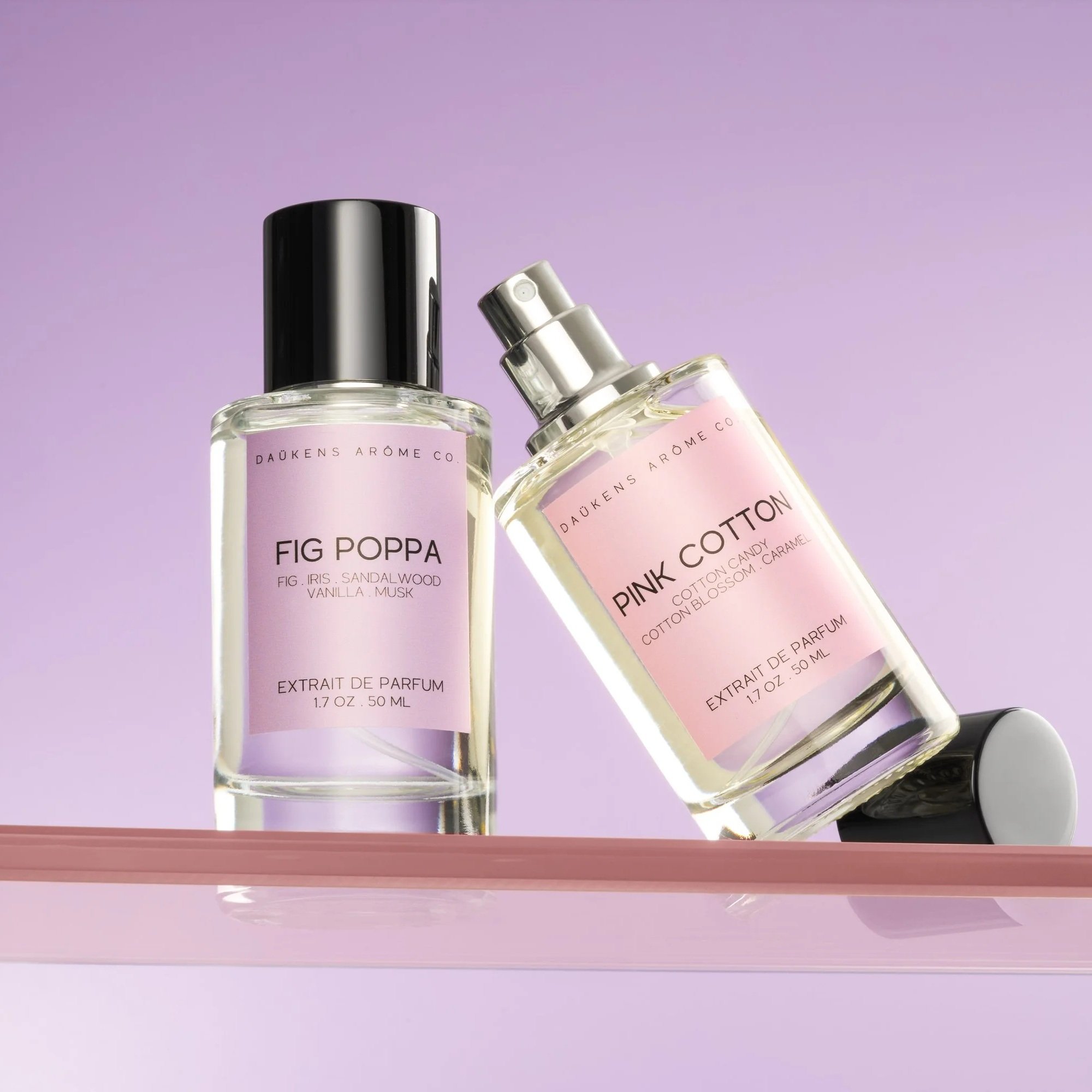 Two perfume bottles on a pink shelf against a purple background. One bottle labeled 'Fig Poppa' and the other 'Pink Cotton,' both with pastel-colored labels.