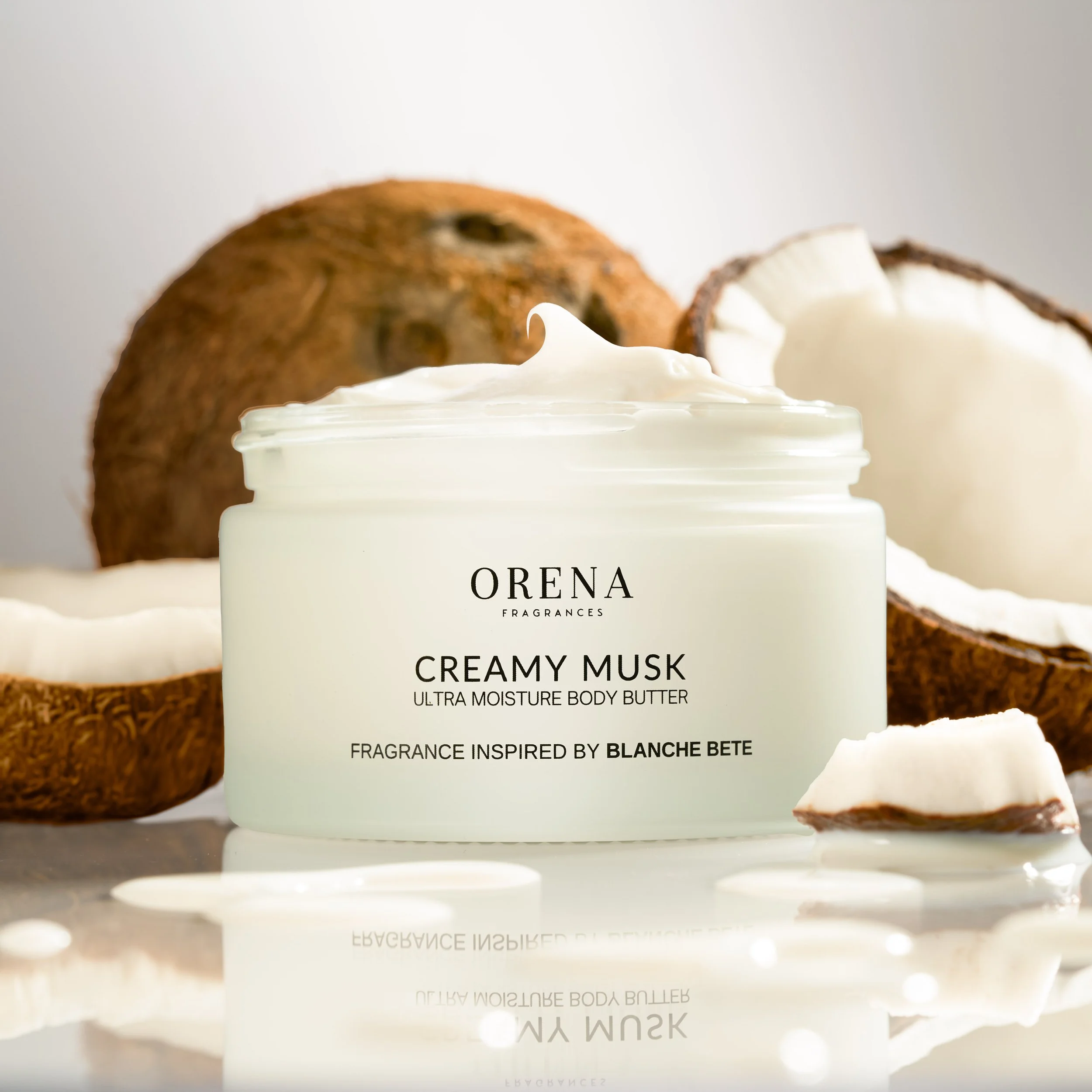 A jar of creamy musk ultra moisture body butter surrounded by pieces of coconut and whole coconuts.