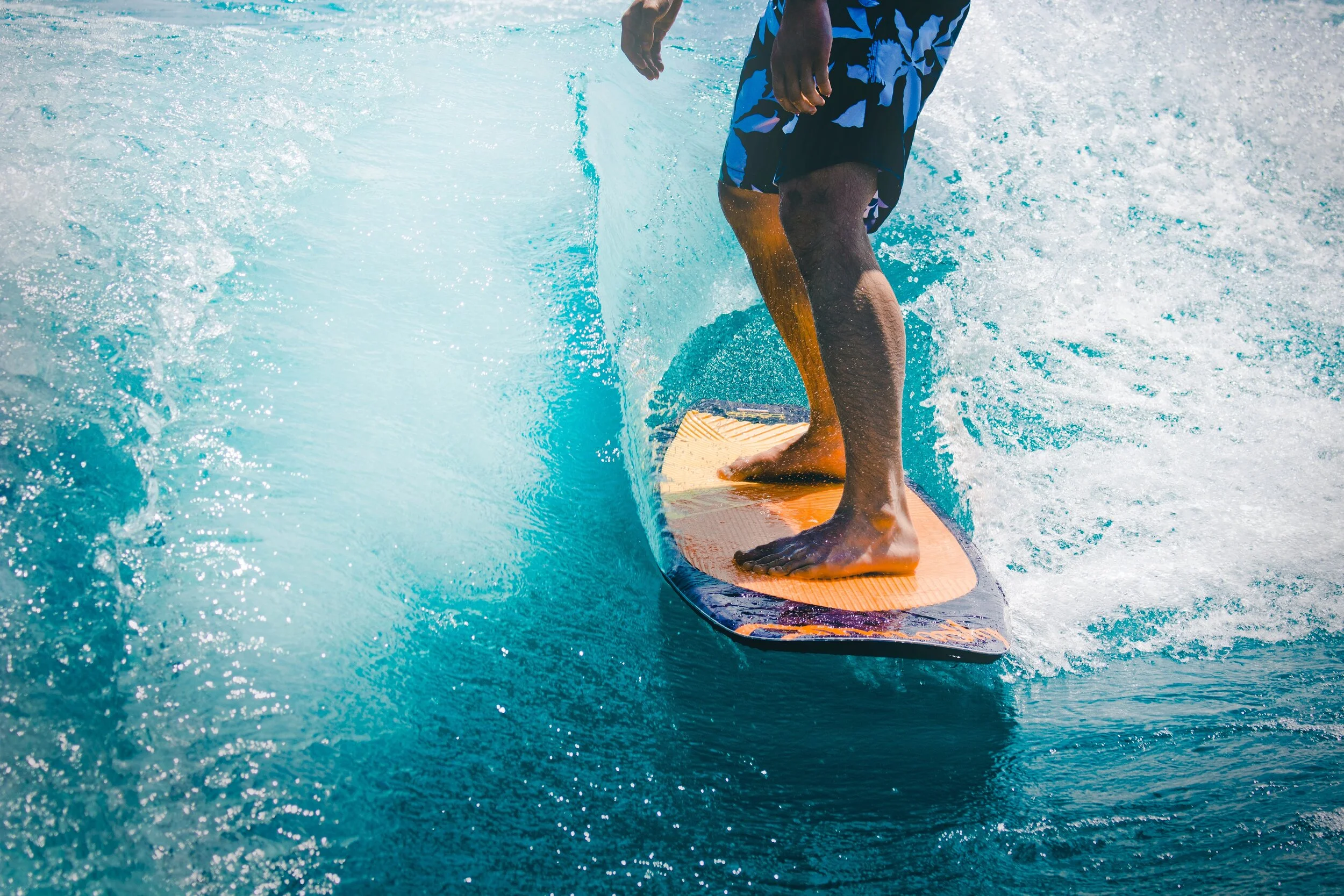 A person riding a jet ski on the water, wearing blue patterned shorts, with one foot forward and one foot back, holding onto the jet ski.