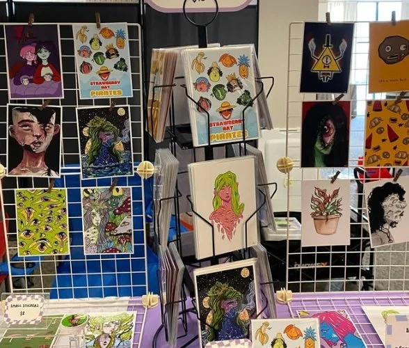 Rack of colorful art prints and cards at a makers market booth