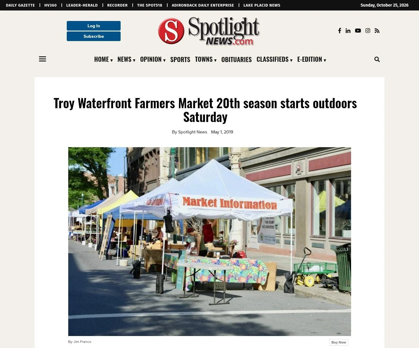 Spotlight News website, May 1, 2019: 'Troy Waterfront Farmers Market 20th season starts outdoors Saturday' by Spotlight News, with a photo by Jim Franco of a row of vendor tents on a downtown Troy street, led by a white Market Information tent.