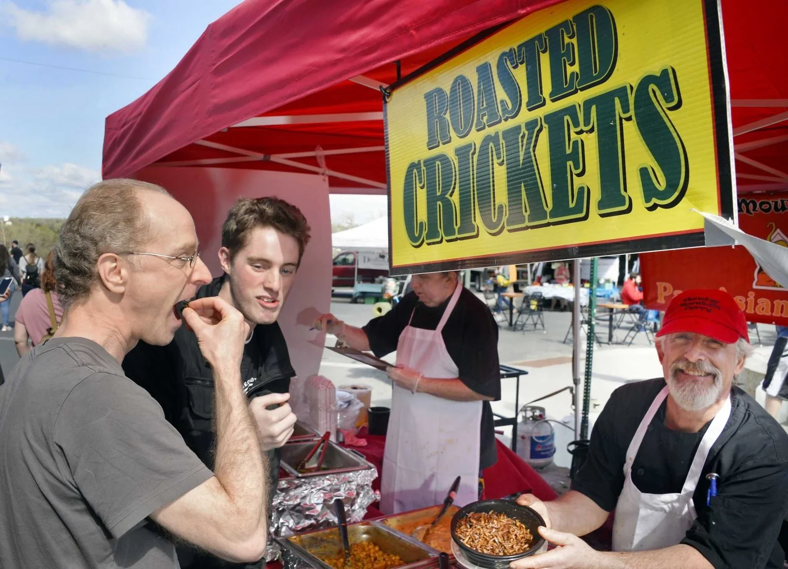 Color photo as published on timesunion.com: Andrew Ashley and his nephew James Ashley sample roasted crickets from Mike Gordon’s booth on River Street at the market’s outdoor opening, May 5, 2018. Photo by John Carl D’Annibale, Times Union.