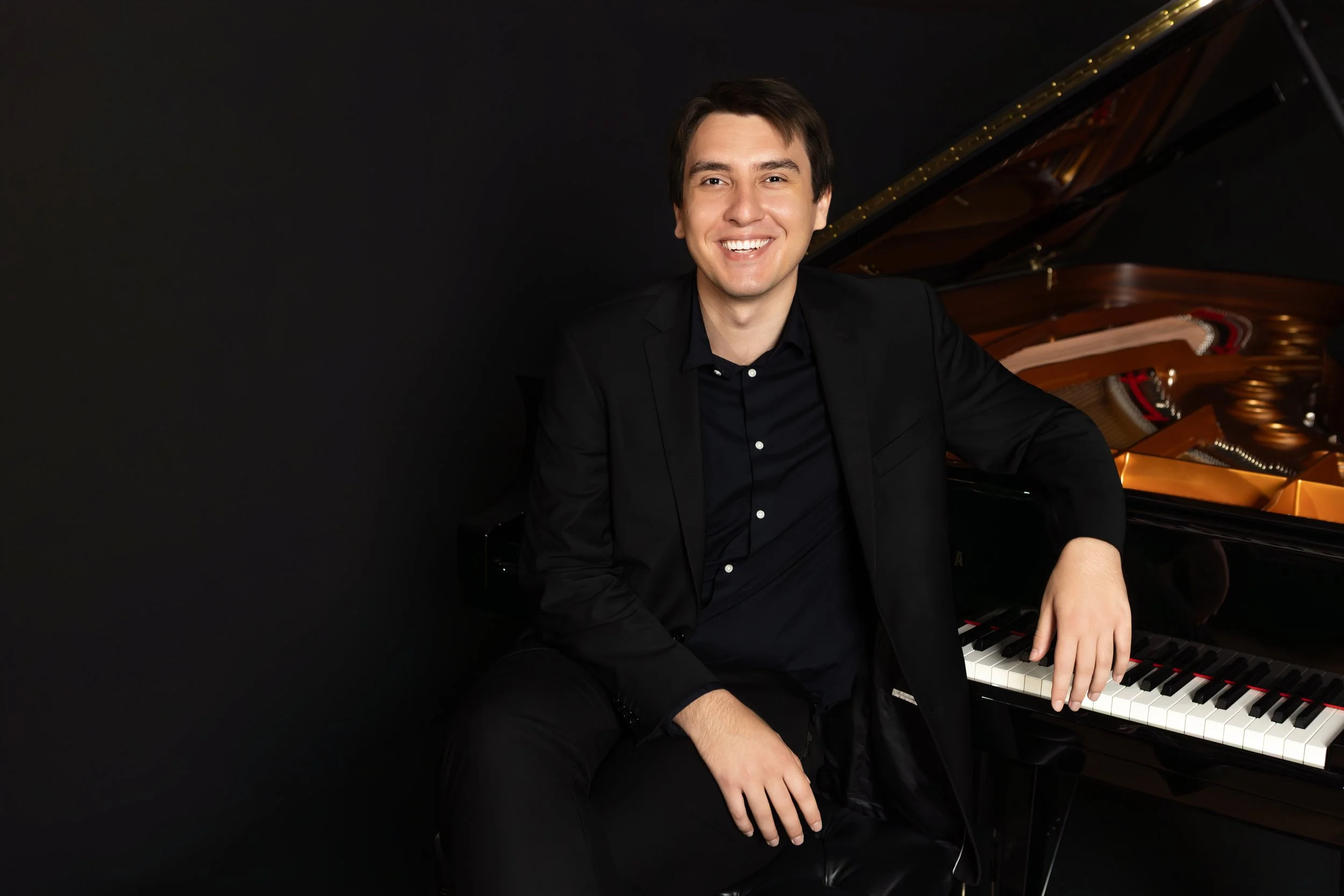 A young man seated next to a grand piano.