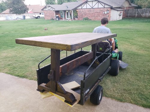 Hauling a new wooden table across the lawn with a riding mower.
