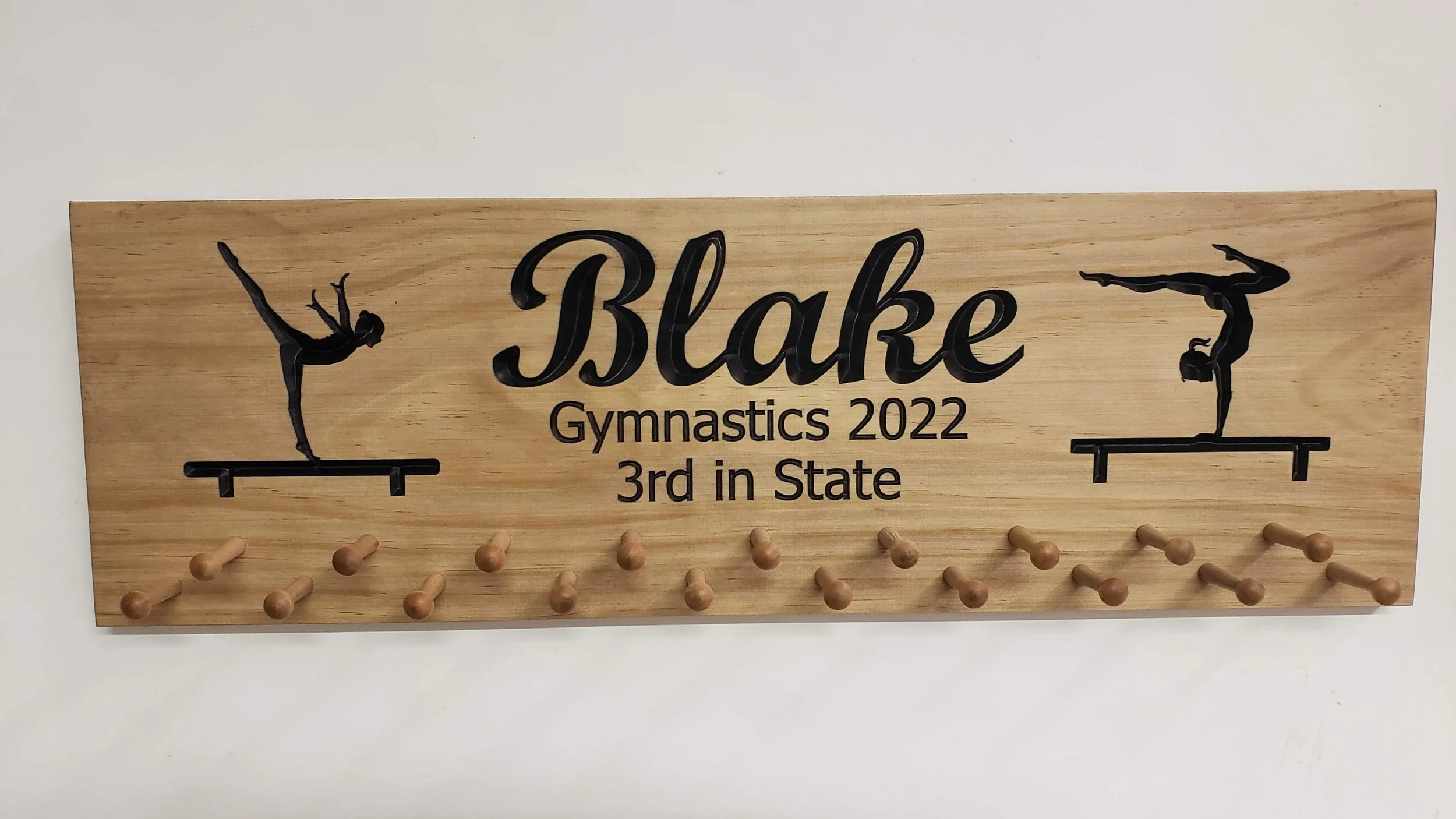 **Short Facebook Post:**

---

🏅 **Custom Gymnastics Medal Display!**

Proudly showcase your gymnast&rsquo;s achievements with this beautiful 23x7" wooden medal holder. Features balance beam silhouettes and custom text &mdash; shown here with &