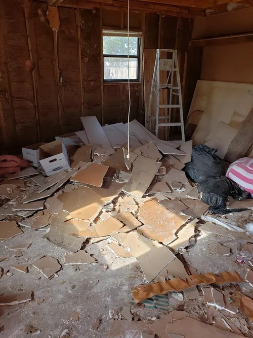 Room under renovation with debris, broken tiles and a ladder.