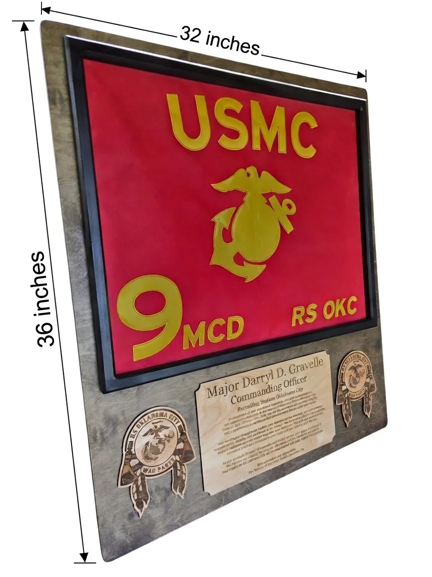 Close-up detail of the lower portion of the USMC guidon plaque, highlighting the laser-engraved "RS Oklahoma City War Party" unit emblems and the personalized engraved plaque with Major Darryl D. Gravelle’s name and retirement message.