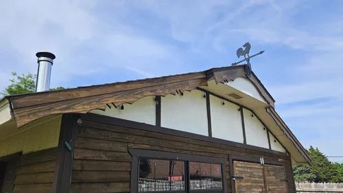Wood-covered gable with a weather vane, chimney and string lights.