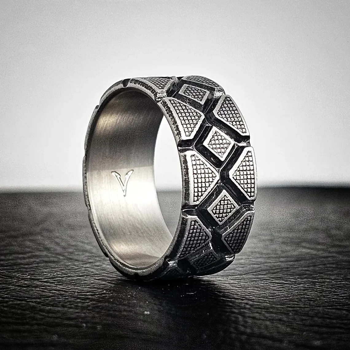 Close-up of battleworn titanium men's wedding ring interior showing polished comfort fit and engraved 'Y' mark, 10mm Diamondback geometric design