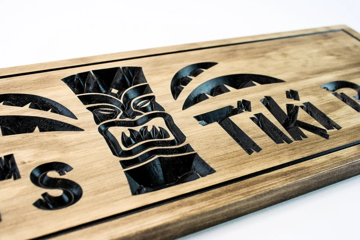 Close-up detail of hand carved wooden Tiki mask with intricate headdress and facial features on custom Tiki Bar sign