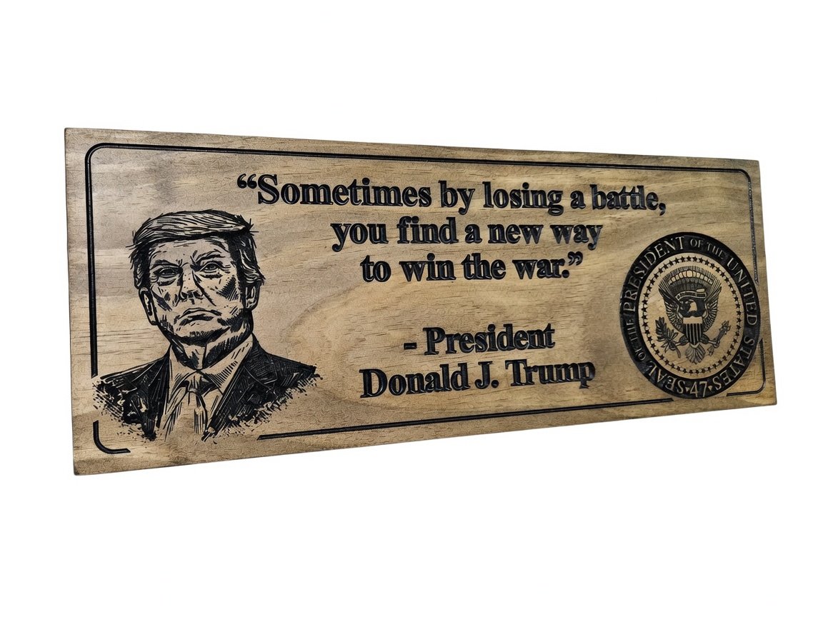 Front view of a 23 x 9 Donald J. Trump wooden wall sign made of pine. Displays a detailed engraved portrait of President Trump, the inspirational quote “Sometimes by losing a battle,.jpg