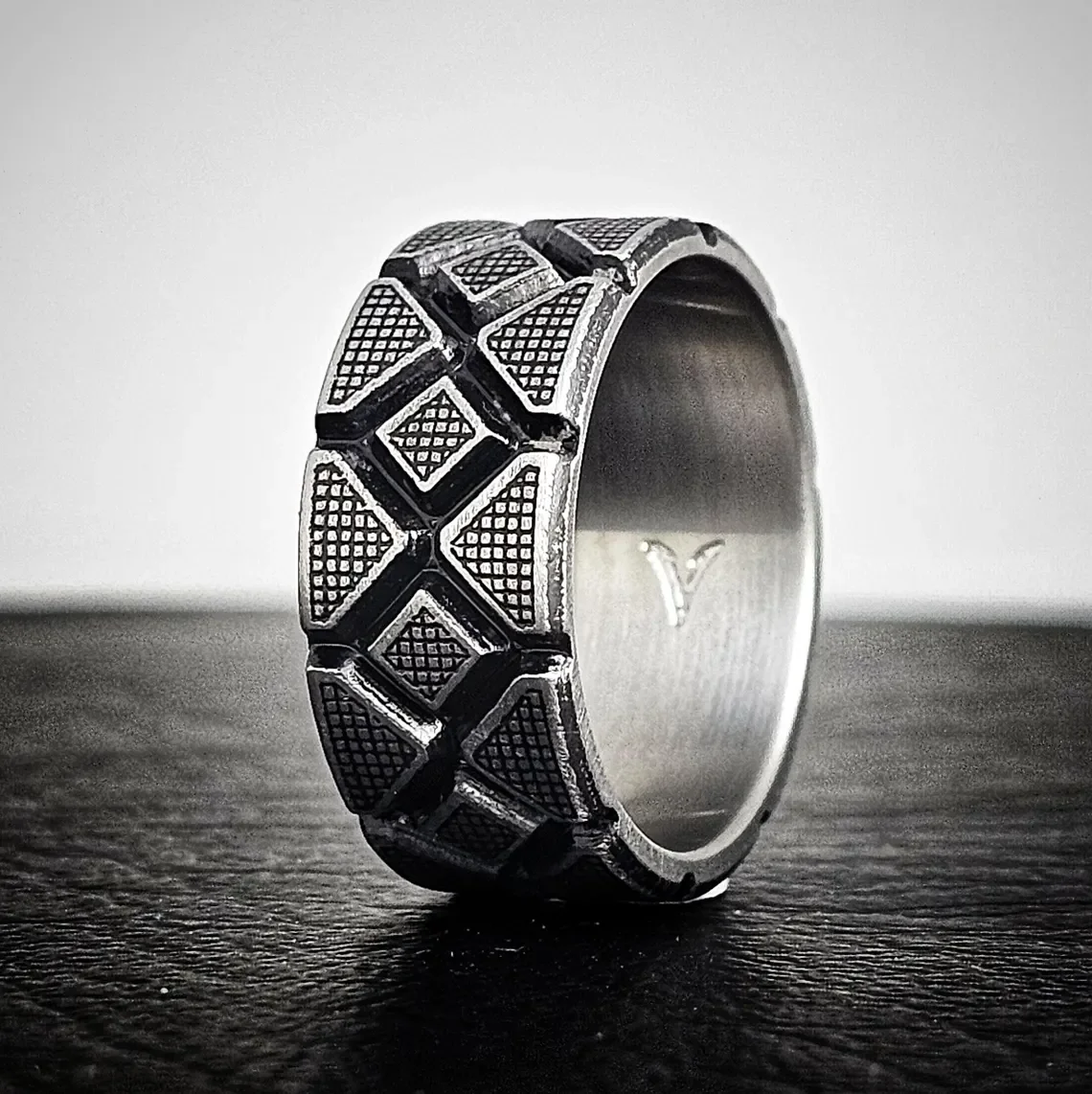 Battleworn titanium wedding ring with geometric Diamondback pattern, 10mm wide men's band in rugged silver finish, shown from angled view on dark background