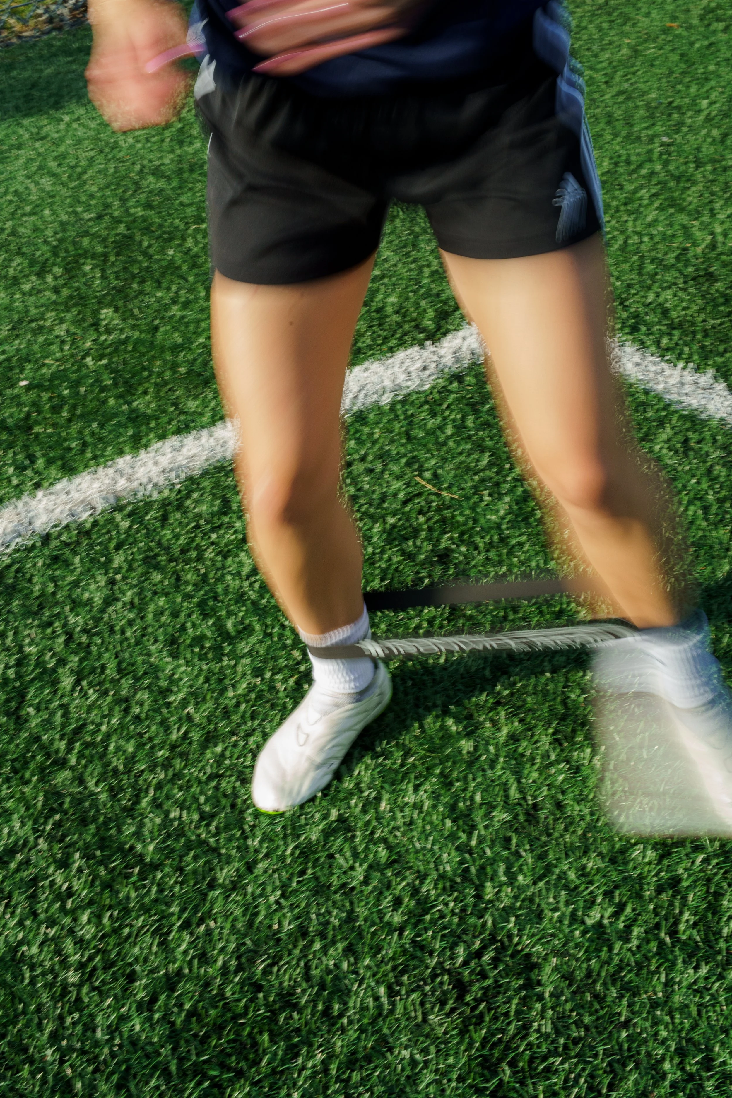 A person in athletic gear, black shorts, white shoes, and white socks, holding a tennis racket on a green turf tennis court.