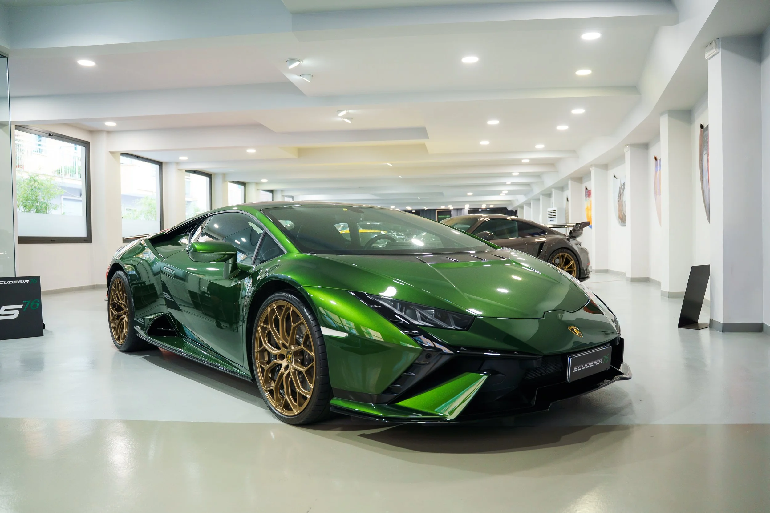 Green Lamborghini sports car on display in showroom with other cars and art on walls.