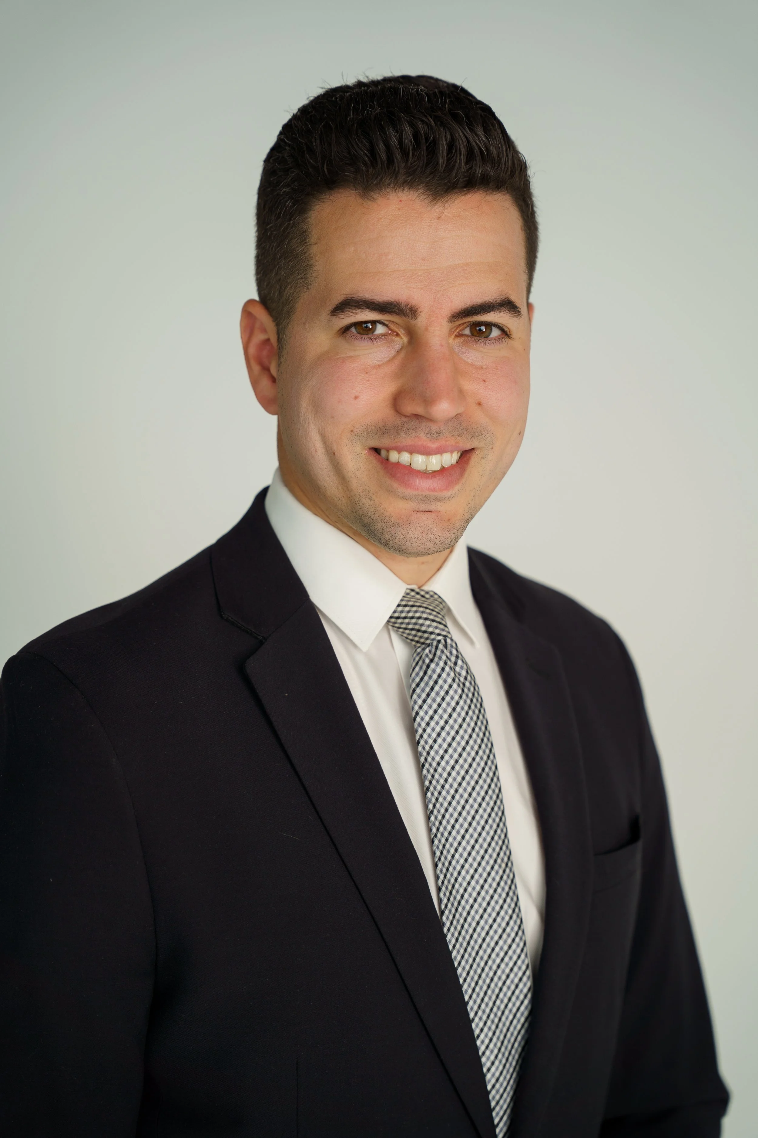 Professional headshot of a smiling man in a suit and tie against a plain background.