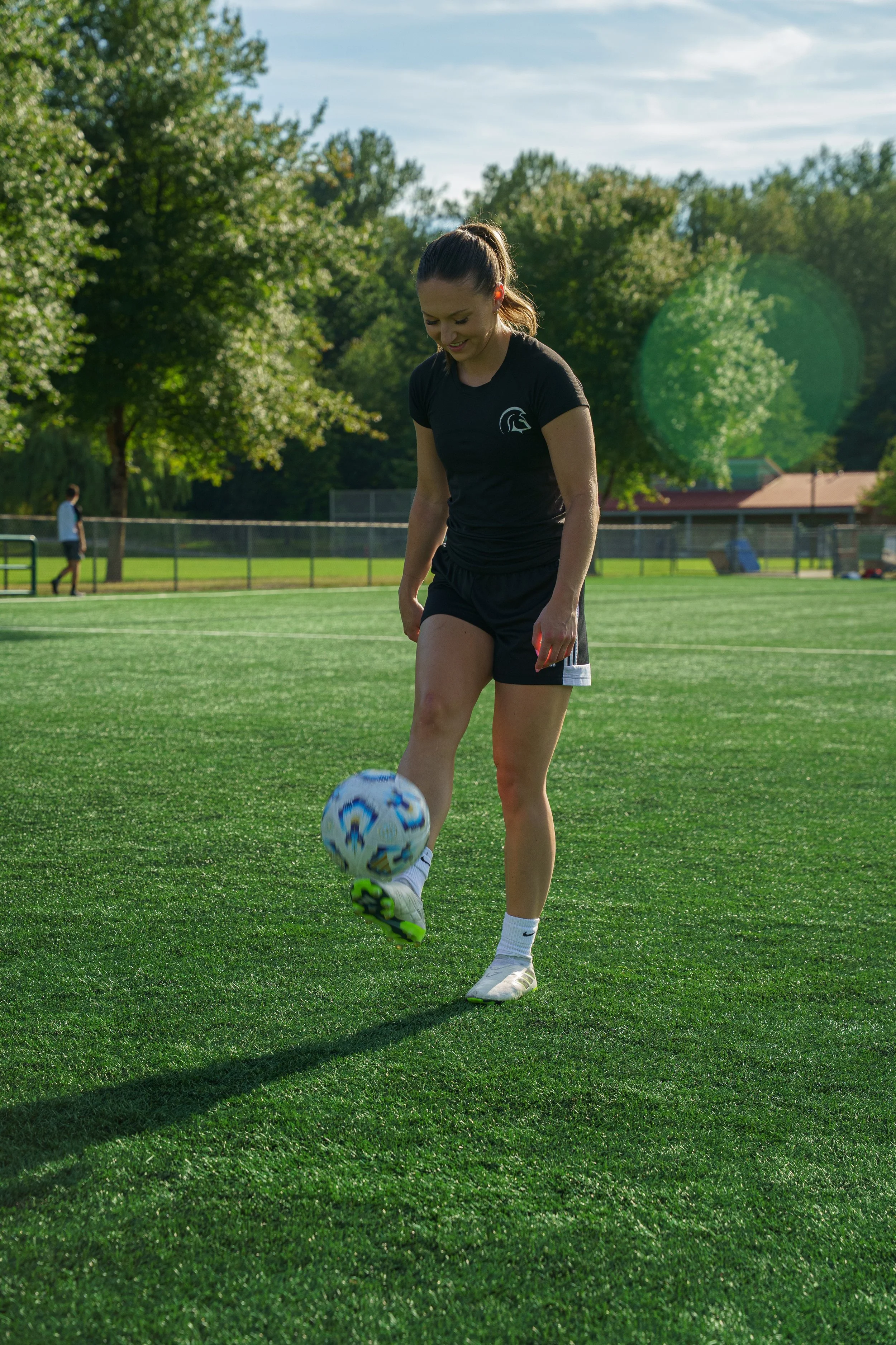 A young woman in black sportswear and white socks playing soccer on a green field in a park.