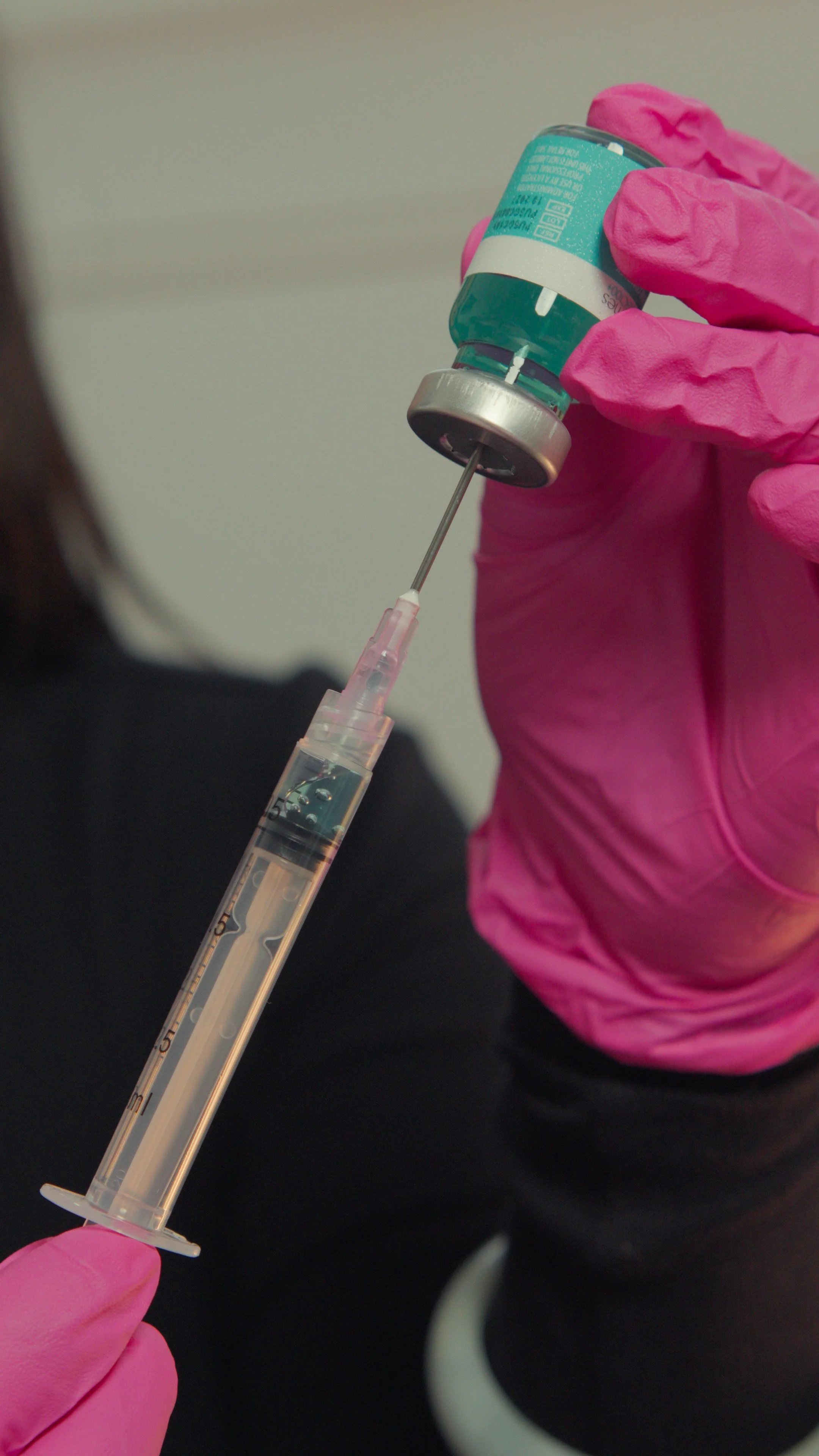 A person wearing pink gloves drawing liquid from a vial into a syringe.