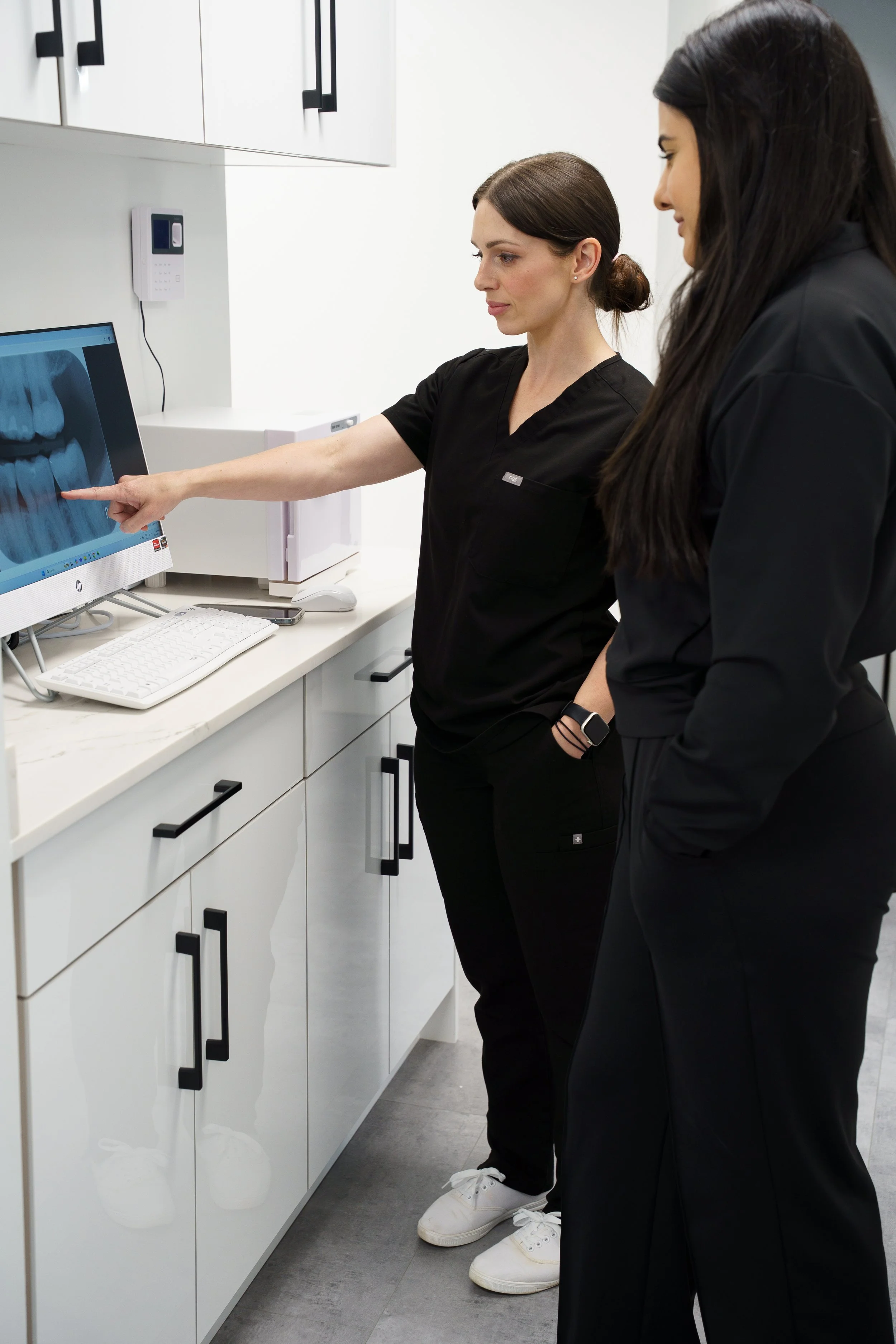 Two dental professionals reviewing and discussing a digital dental x-ray on a computer monitor in a clinical setting