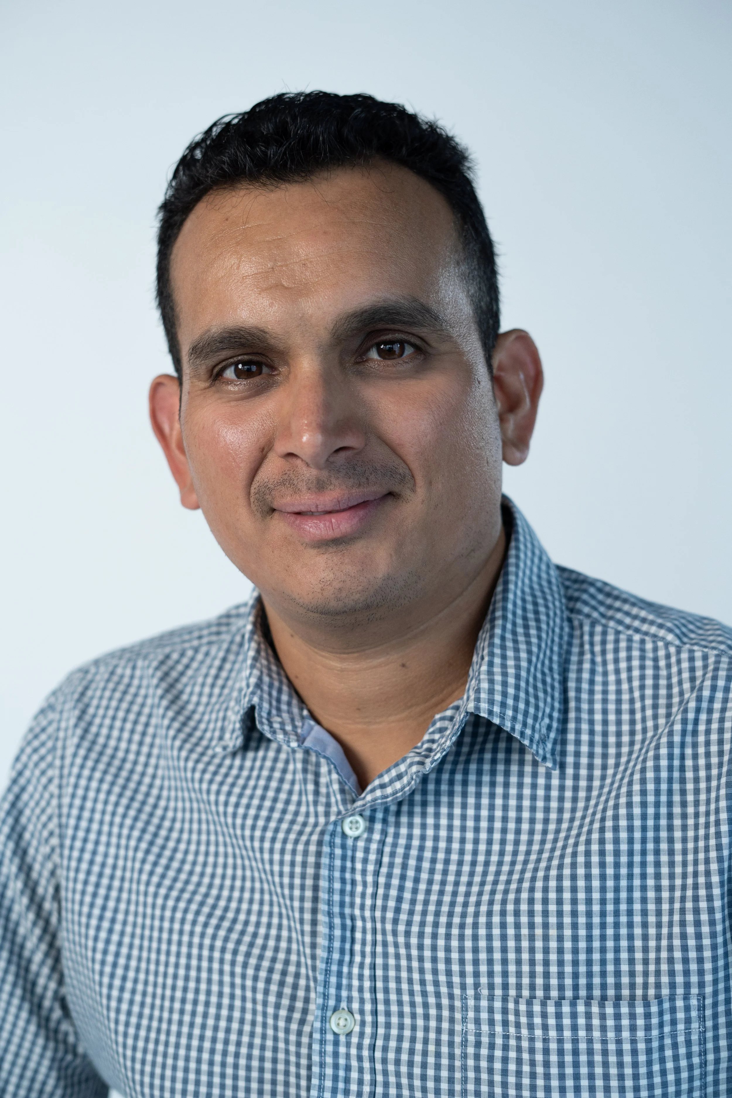 Headshot of a man in a checkered shirt smiling, with a plain white background.
