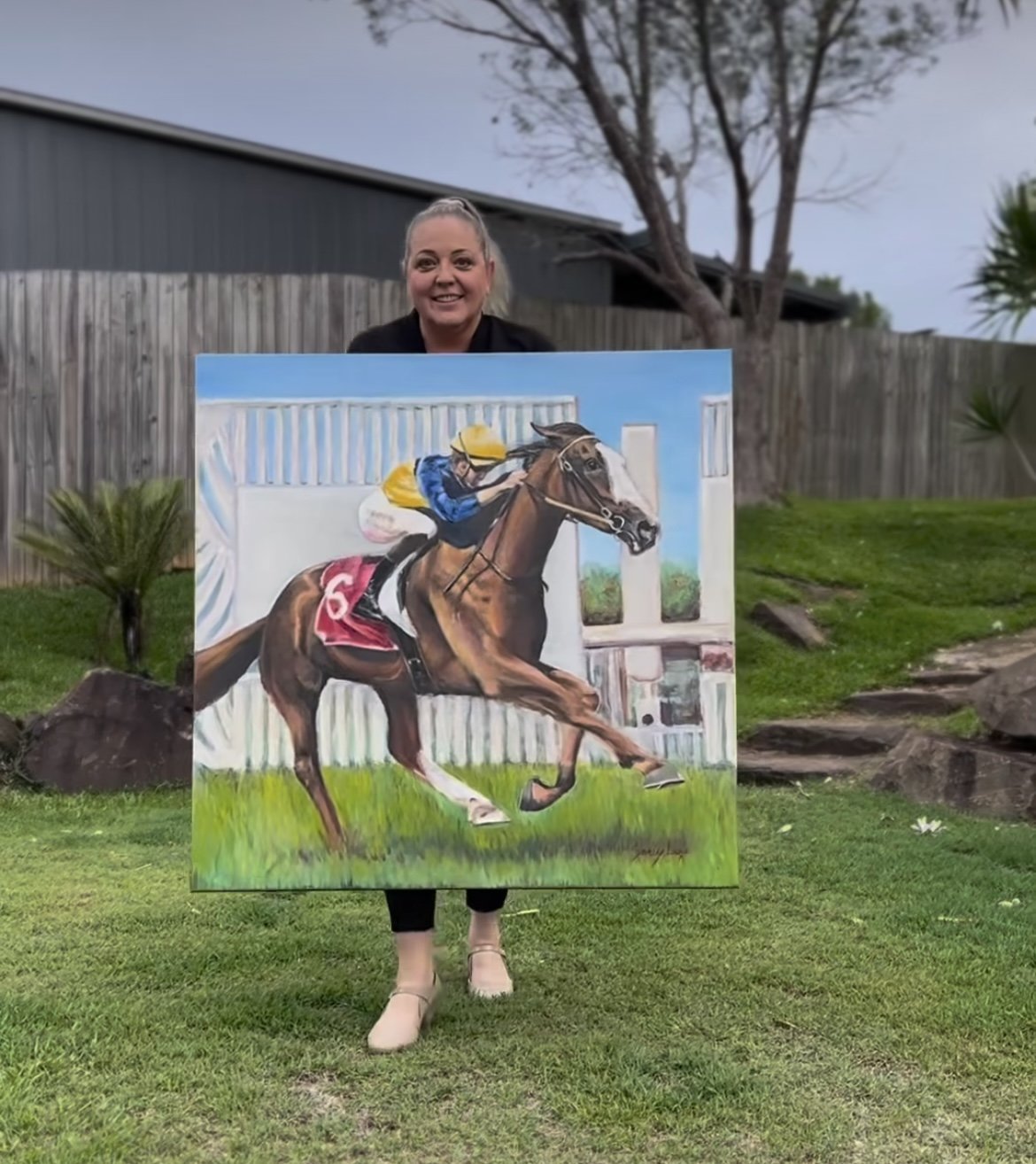 Sandy Lee Artistry holding her original oil painting of racehorse Abounding and jockey Ben Thompson winning at the Sunshine Coast.