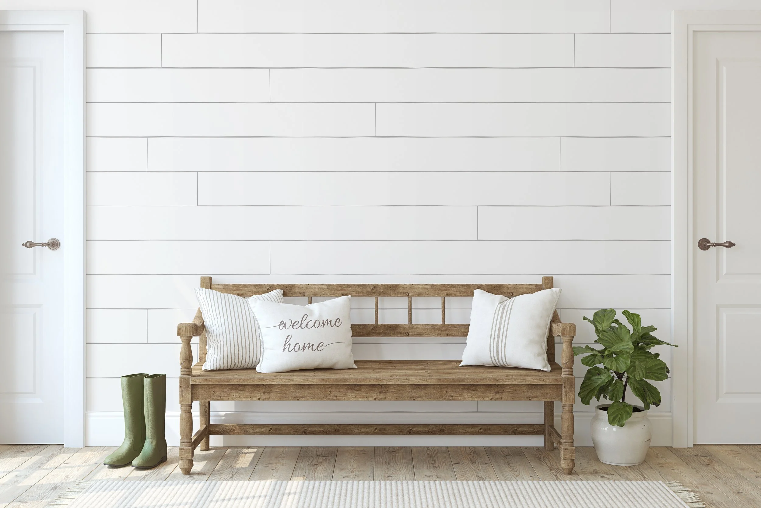 Interior entryway with a wooden bench, decorative pillows, green rain boots, a potted houseplant, white shiplap walls, and two closed white doors.