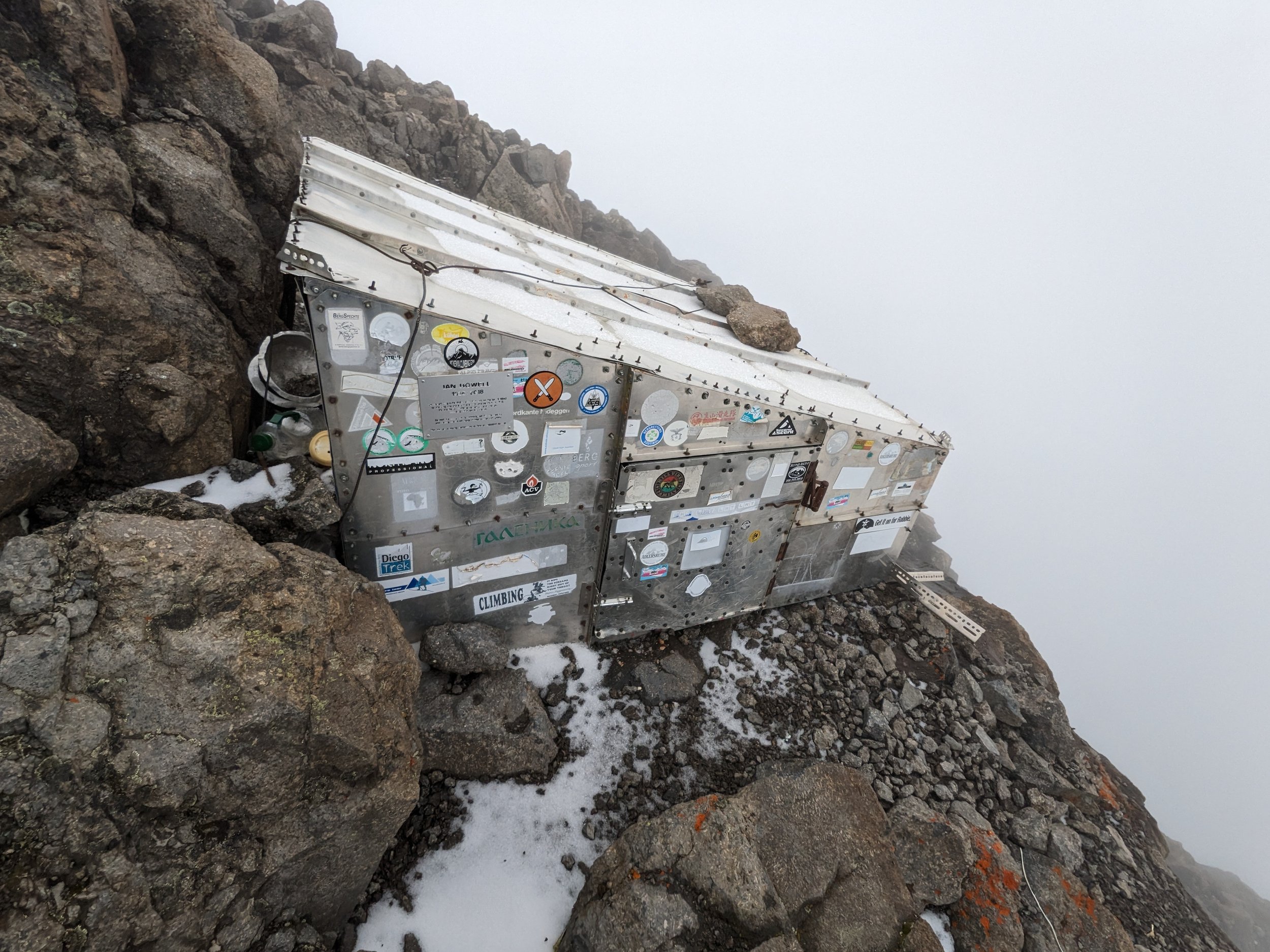 Climber's rescue device attached to a rocky mountain slope, with snow and foggy weather.