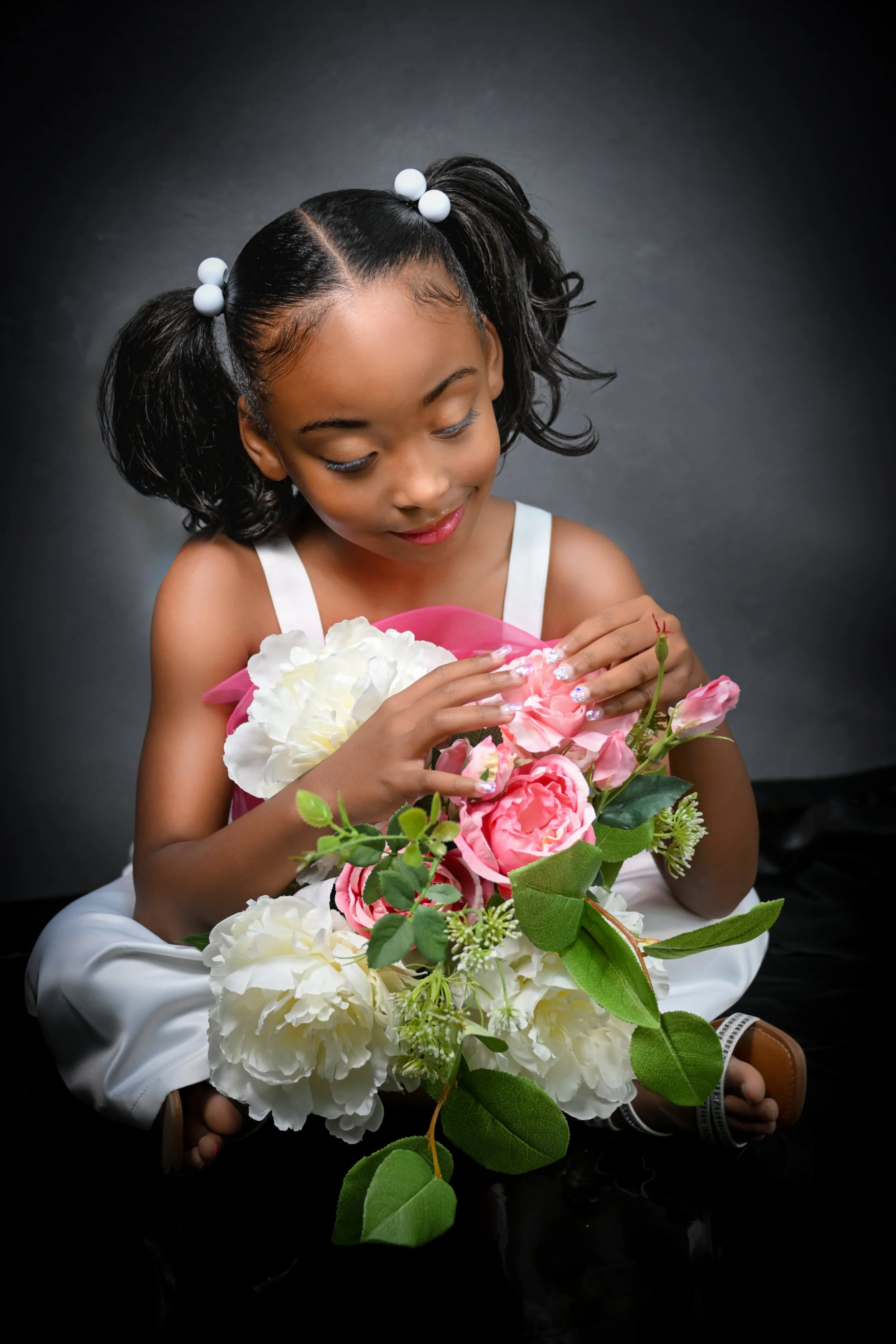 Little girl sits on the floor and plays with vase of flowers for Mother's Day photo shoot